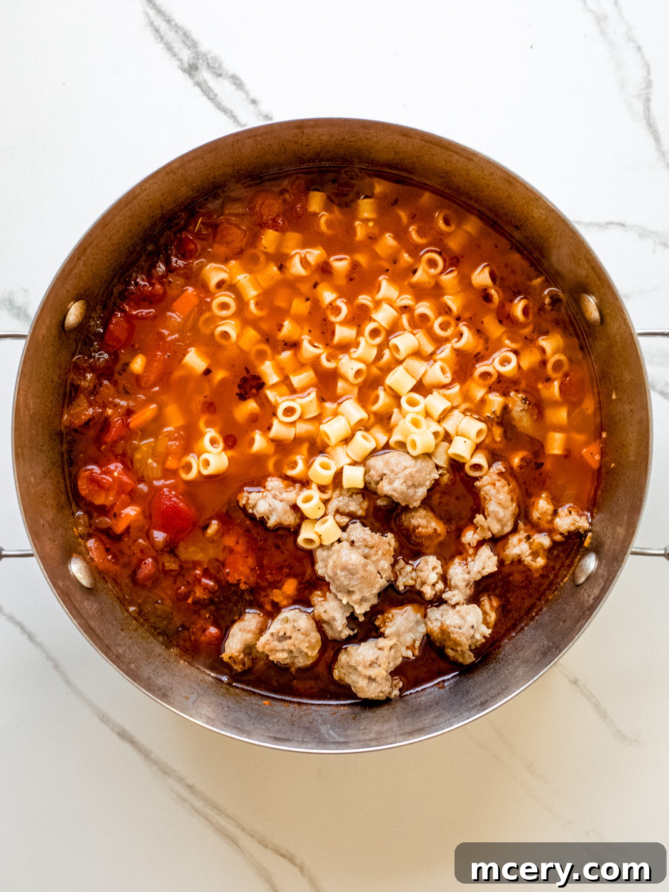 Hearty Italian Sausage Soup 6 Cooked sausage and pasta added to the simmering soup broth in a pot.