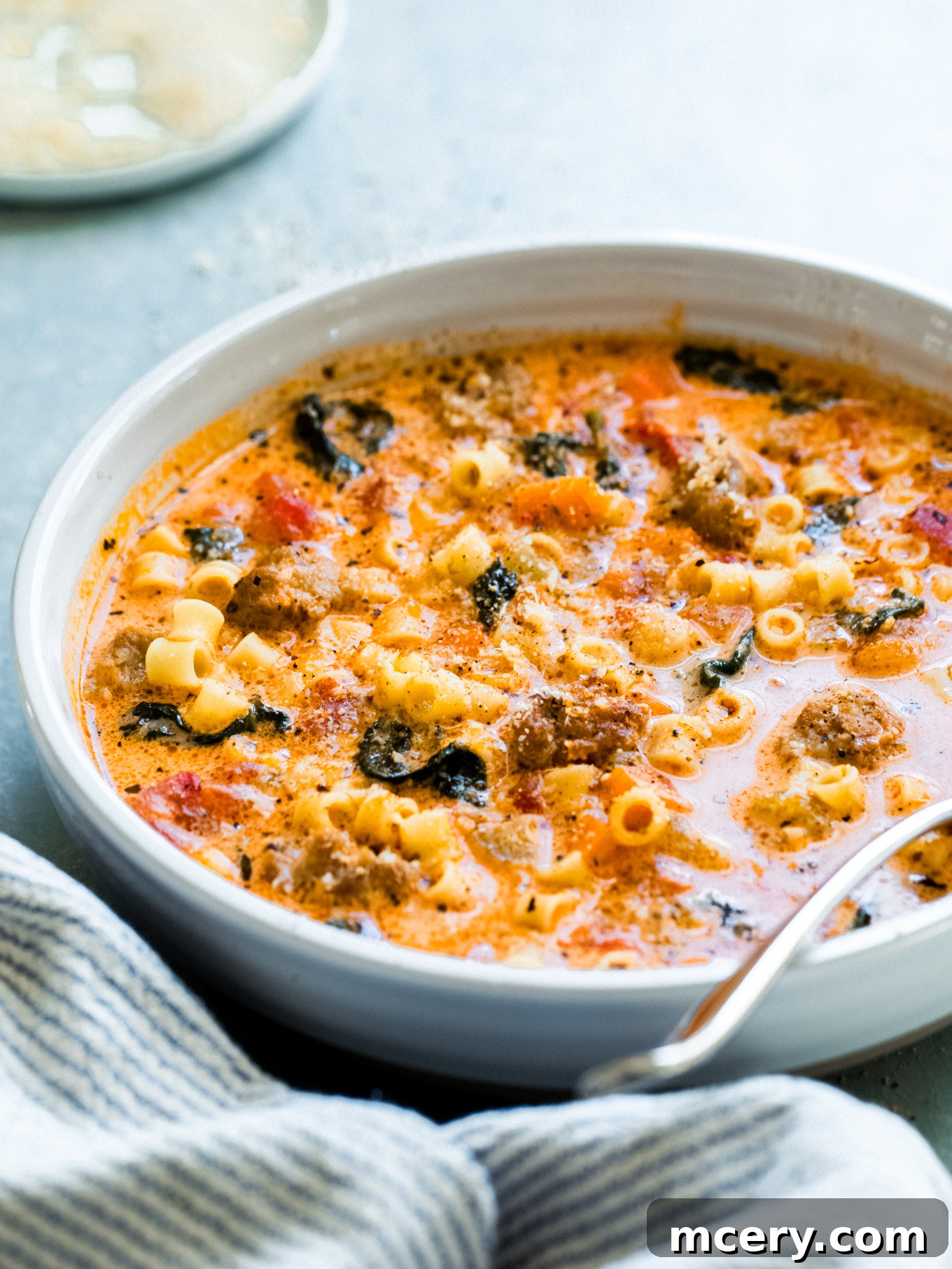 Hearty Italian Sausage Soup 10 A close-up of Italian sausage soup in a bowl with a spoon, highlighting its creamy texture and hearty ingredients.