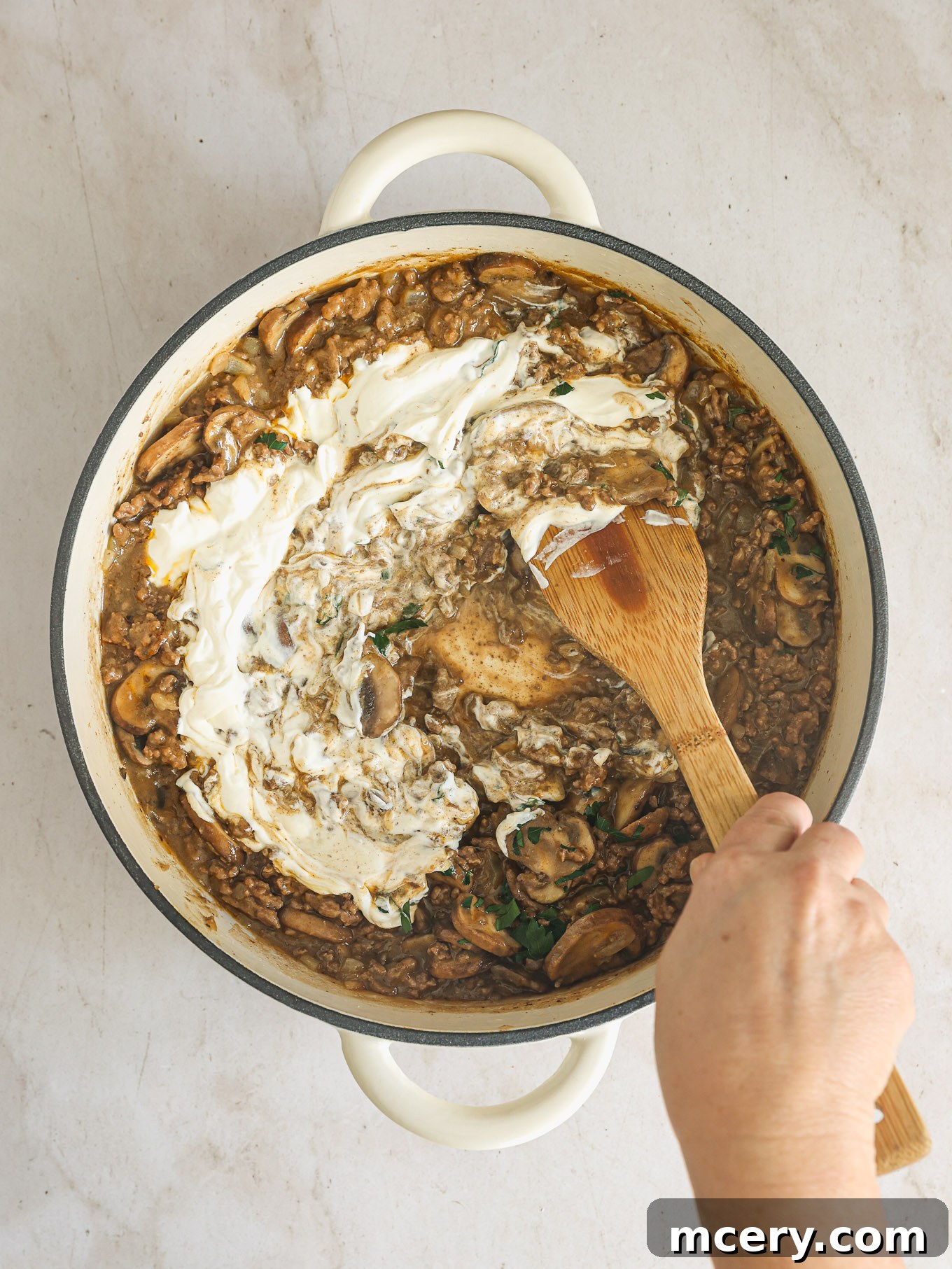 No-Fuss Beef Stroganoff 9 Sour cream being stirred into the beef and mushroom mixture in a skillet off the heat.