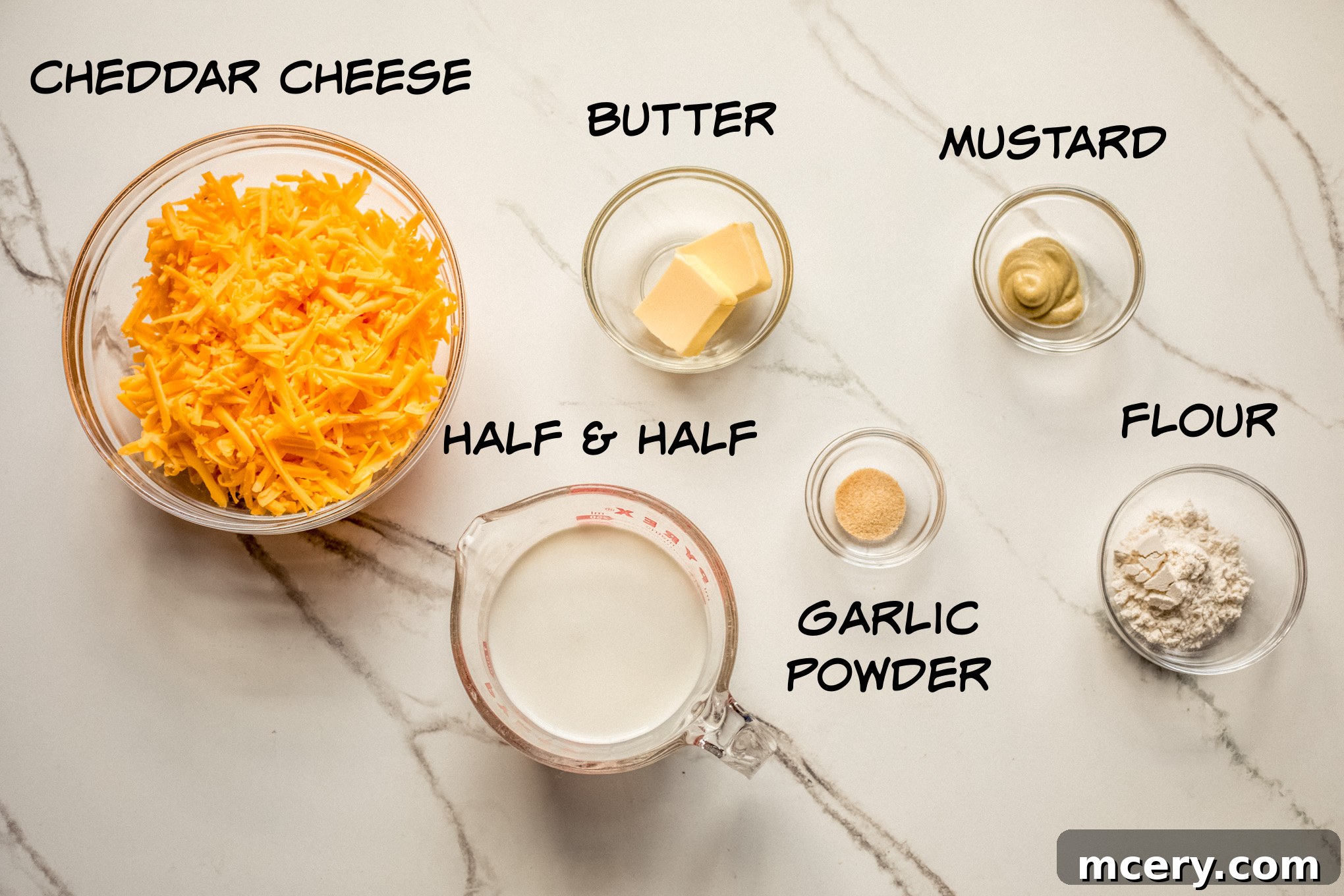 Velvety Smooth Cheese Sauce 3 All ingredients for homemade cheese sauce recipe laid out on a white surface, including butter, flour, half and half, Dijon mustard, spices, and a block of cheddar cheese.