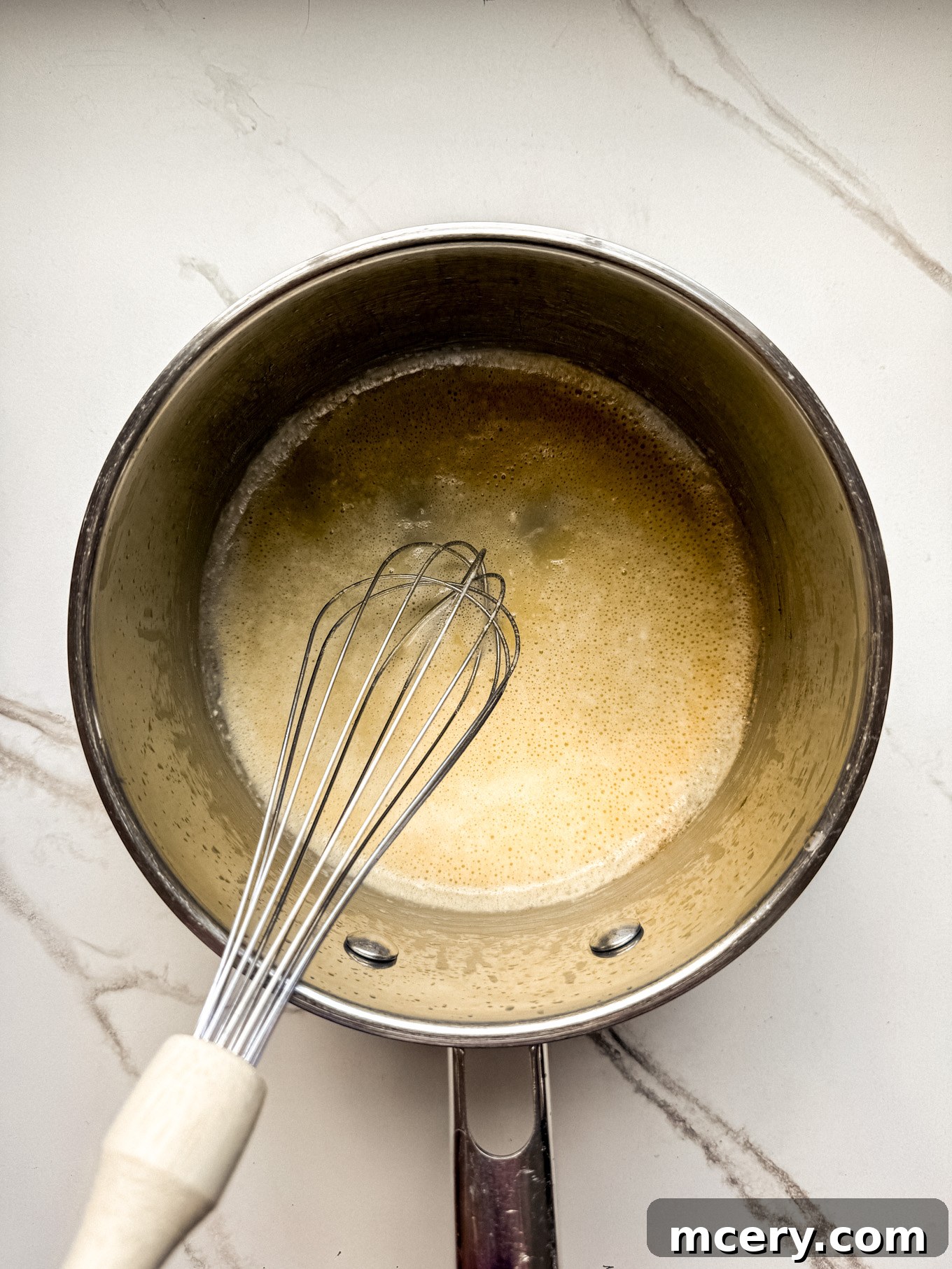 Velvety Smooth Cheese Sauce 4 Melted butter and flour being whisked together in a saucepan to form a roux.