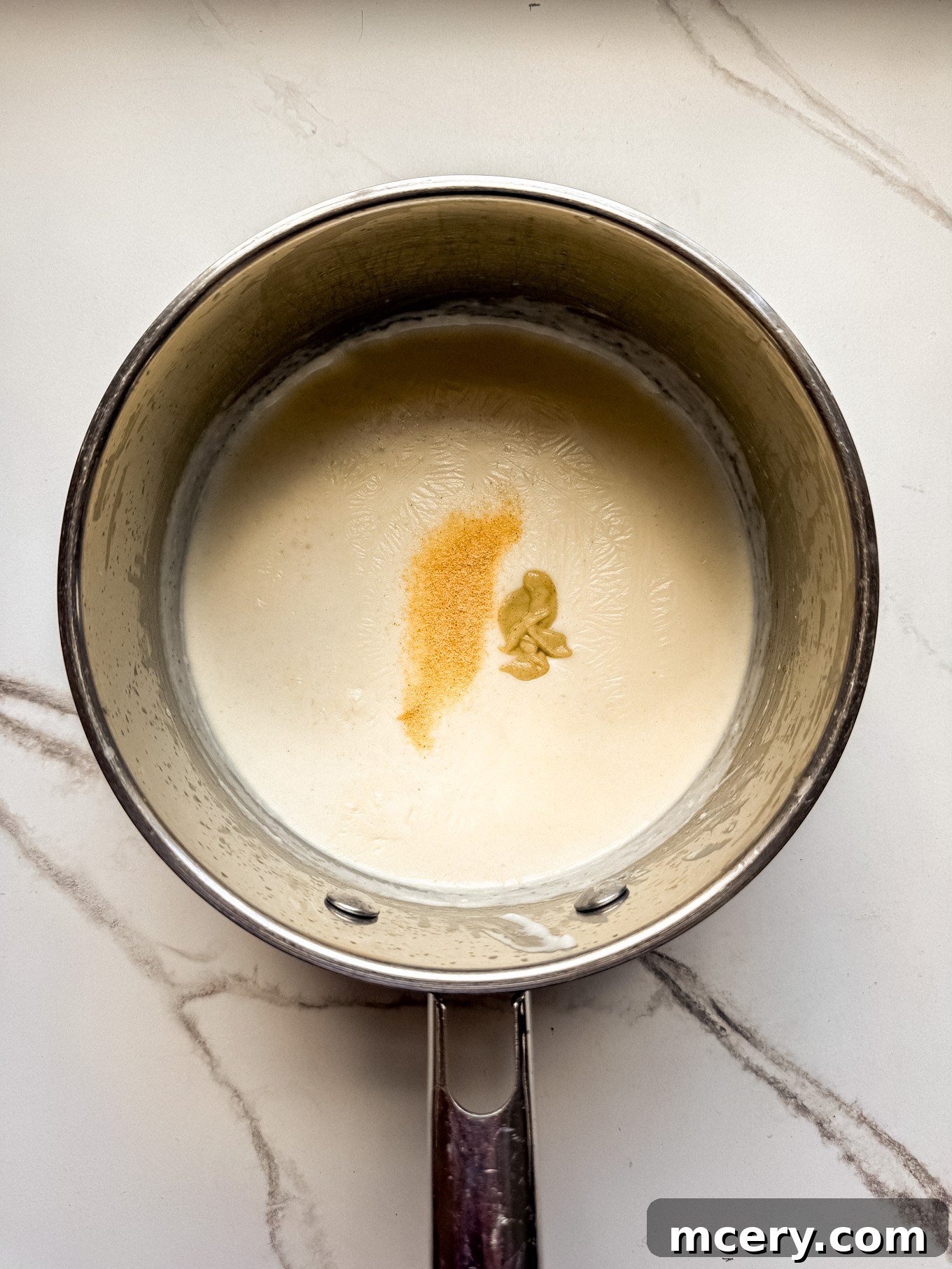 Velvety Smooth Cheese Sauce 6 Dijon mustard and garlic powder added to the thickening cream mixture in a saucepan.