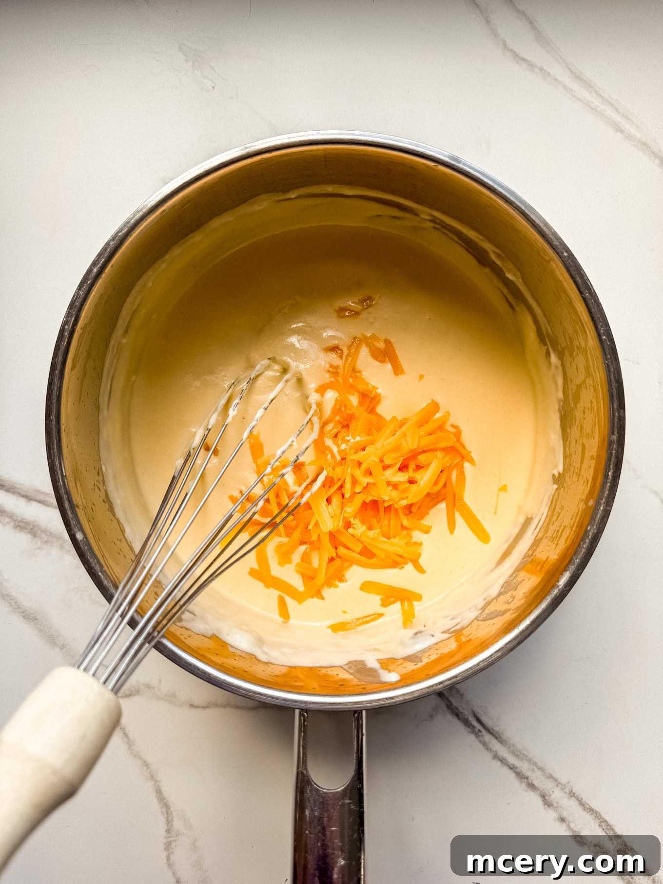 Velvety Smooth Cheese Sauce 7 Grated cheddar cheese being whisked into the creamy sauce base in a saucepan until smooth.