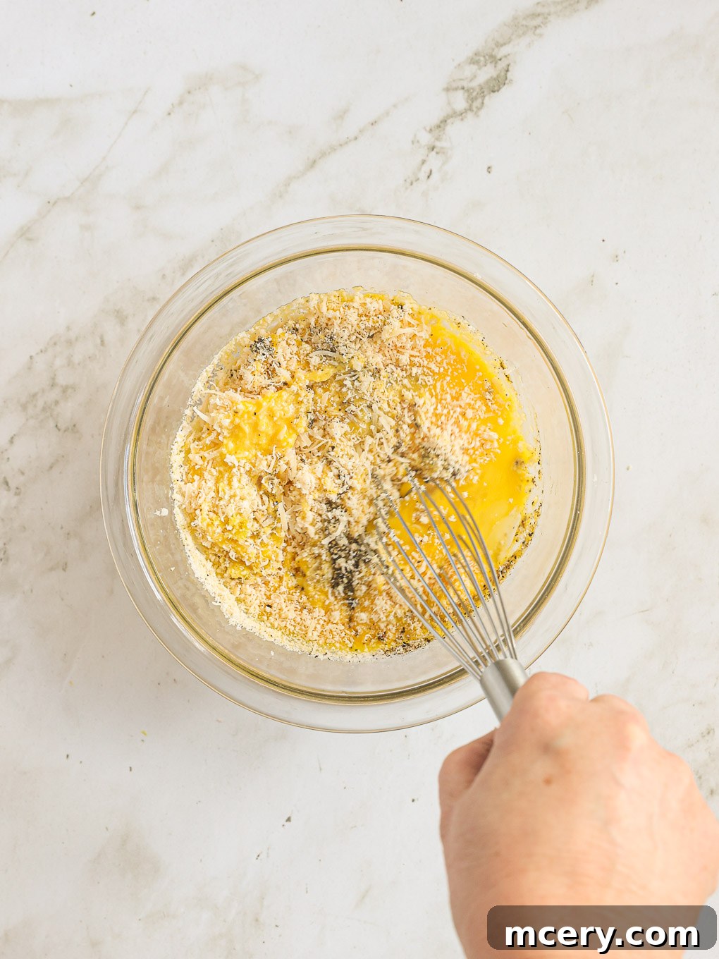 Whisked eggs, Parmesan cheese, lemon zest, lemon juice, and black pepper in a glass bowl with a small amount of pasta water.