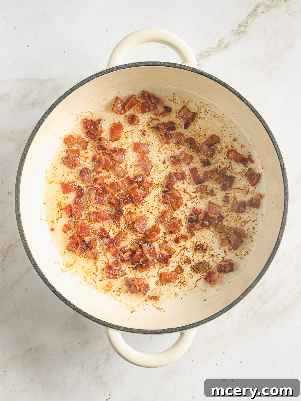 Crispy diced bacon cooking in a large skillet, rendering its fat.