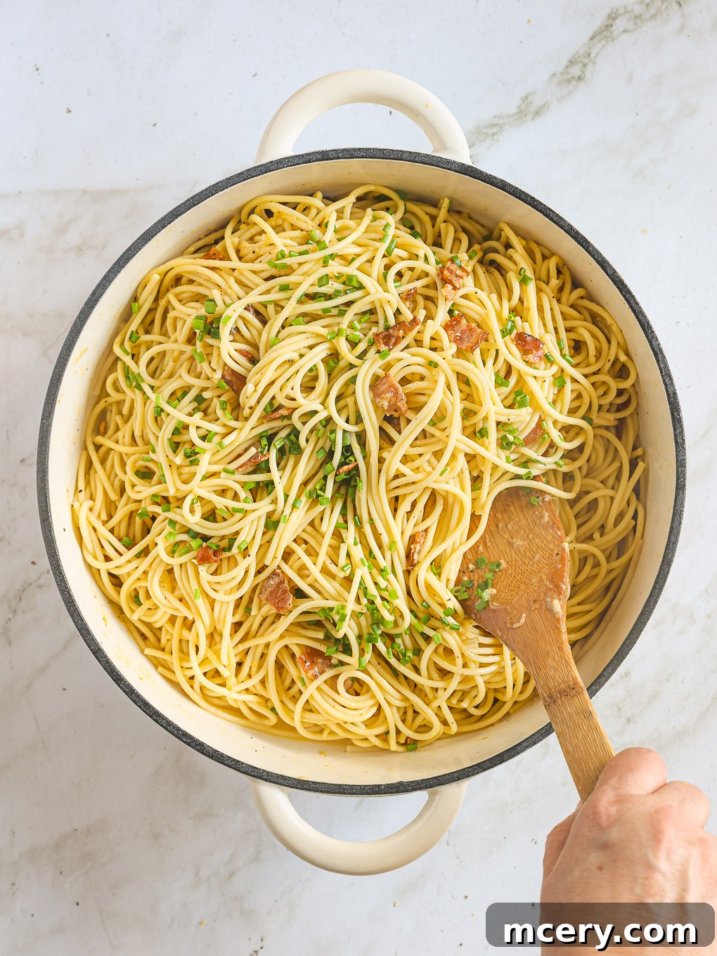 Finished spaghetti carbonara tossed with fresh green herbs in a pan.