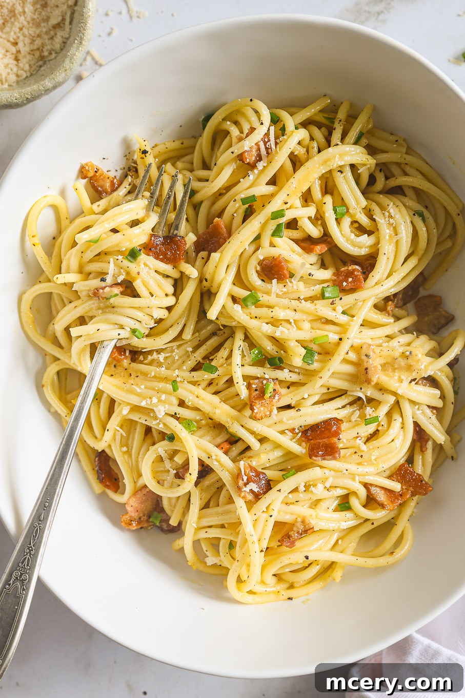 A bowl of creamy lemon herb carbonara spaghetti with a fork, garnished with fresh herbs and black pepper, ready to be eaten.