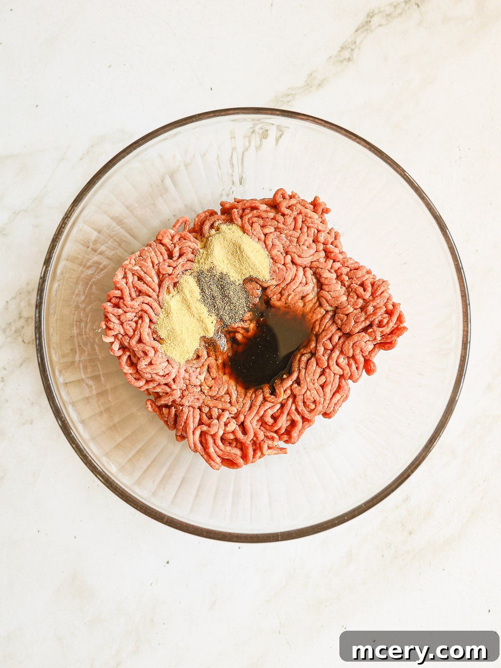 Crafting the Ultimate Homemade Burger 4 Ground beef mixed with a blend of spices and Worcestershire sauce in a glass mixing bowl, ready to be combined.