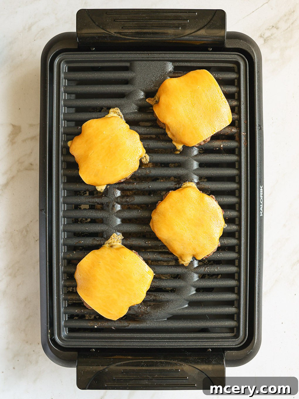 Crafting the Ultimate Homemade Burger 9 Two beef patties cooking on a hot griddle, one topped with melting cheese, demonstrating the grilling process.