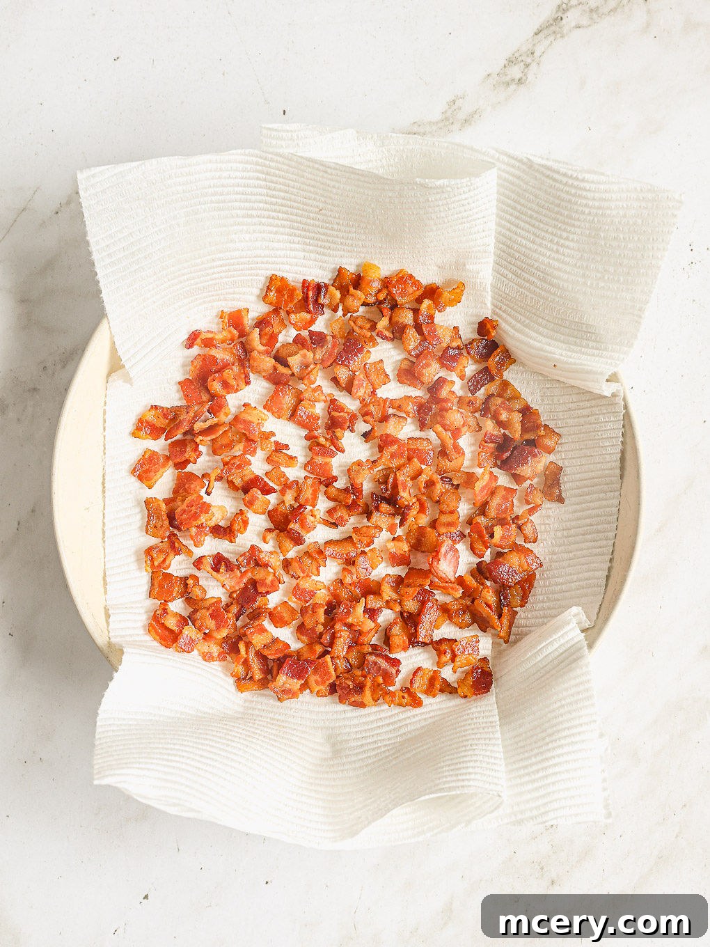 Efsane Hamursuz Kiş Tarifi 5 Cooked, crispy bacon resting on a paper towel-lined plate, with a small amount of rendered bacon grease remaining in the skillet.