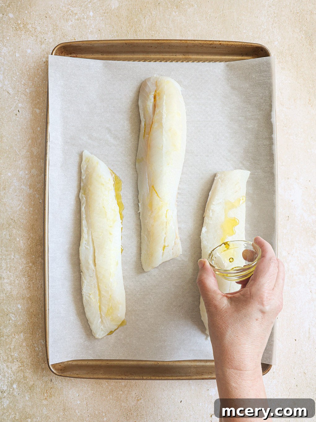 The Ultimate Homemade Fish Tacos 5 Cod fillets arranged on a parchment paper-lined baking sheet, drizzled with olive oil.