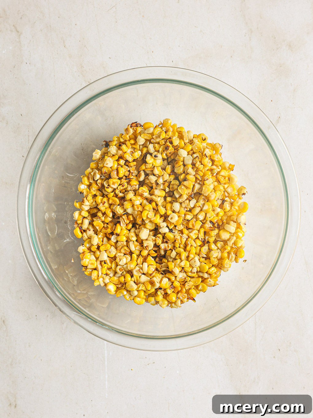 Delicious Mexican Corn Salad From Scratch 5 Charred corn kernels in a clear glass mixing bowl, cooling down after being cooked in a skillet.