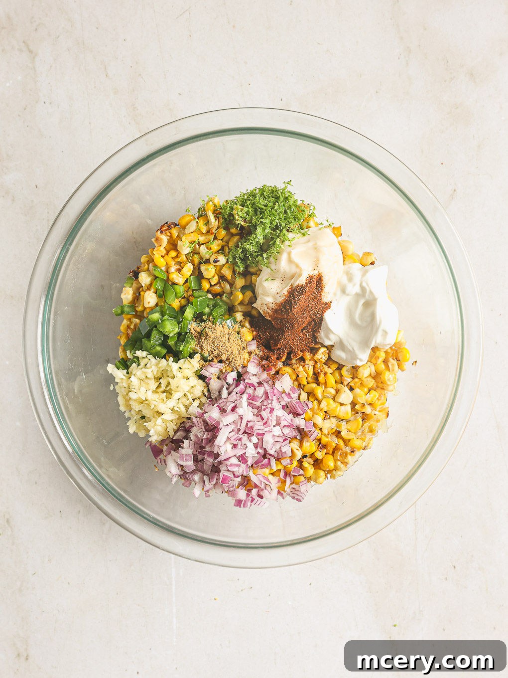 Delicious Mexican Corn Salad From Scratch 6 All the ingredients for Mexican corn salad, including charred corn, diced jalapeños, red onion, and creamy dressing, combined in a glass bowl.