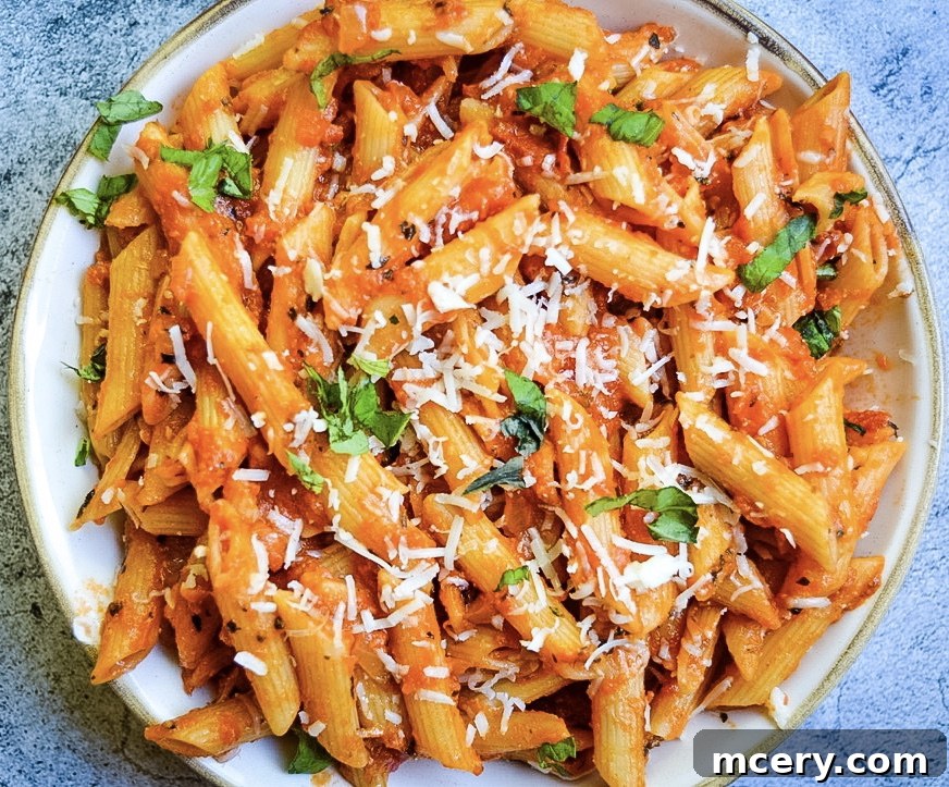 A vibrant close-up of Penne Alla Vodka in a pan, showcasing the rich tomato-cream sauce clinging to the perfectly cooked penne pasta. Fresh basil leaves and grated cheese are sprinkled on top, emphasizing its deliciousness and inviting texture.
