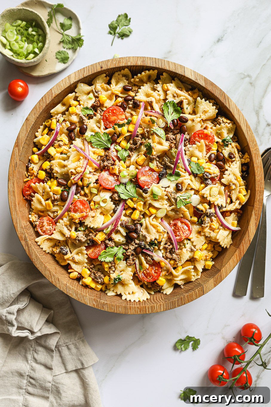 A large wooden bowl filled with creamy Cowboy Pasta Salad, showcasing the pasta, seasoned ground beef, corn, black beans, cherry tomatoes, and a rich, zesty dressing.