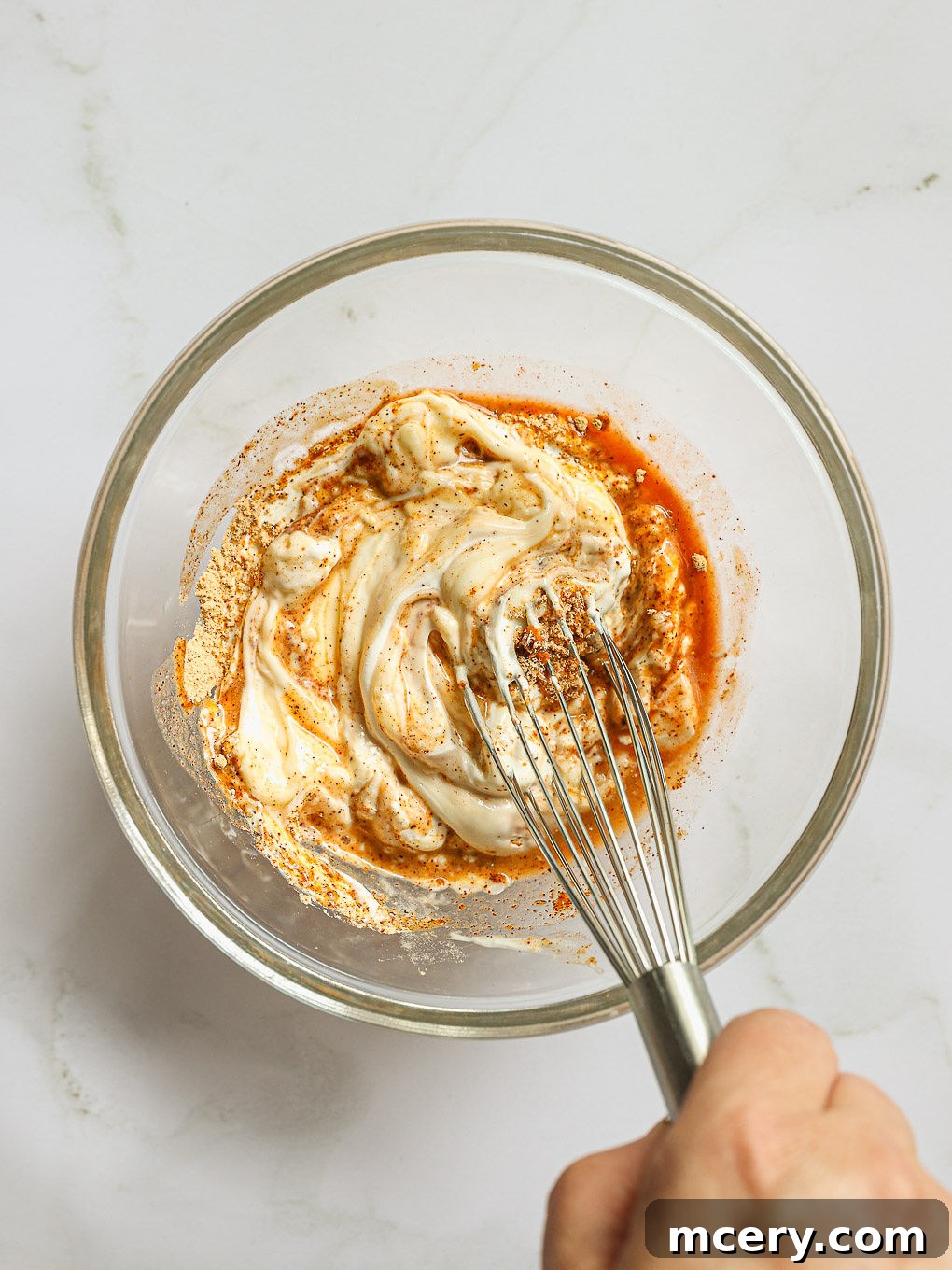 A clear glass bowl containing the creamy dressing ingredients for Cowboy Pasta Salad, smoothly whisked and ready to be combined with the salad.