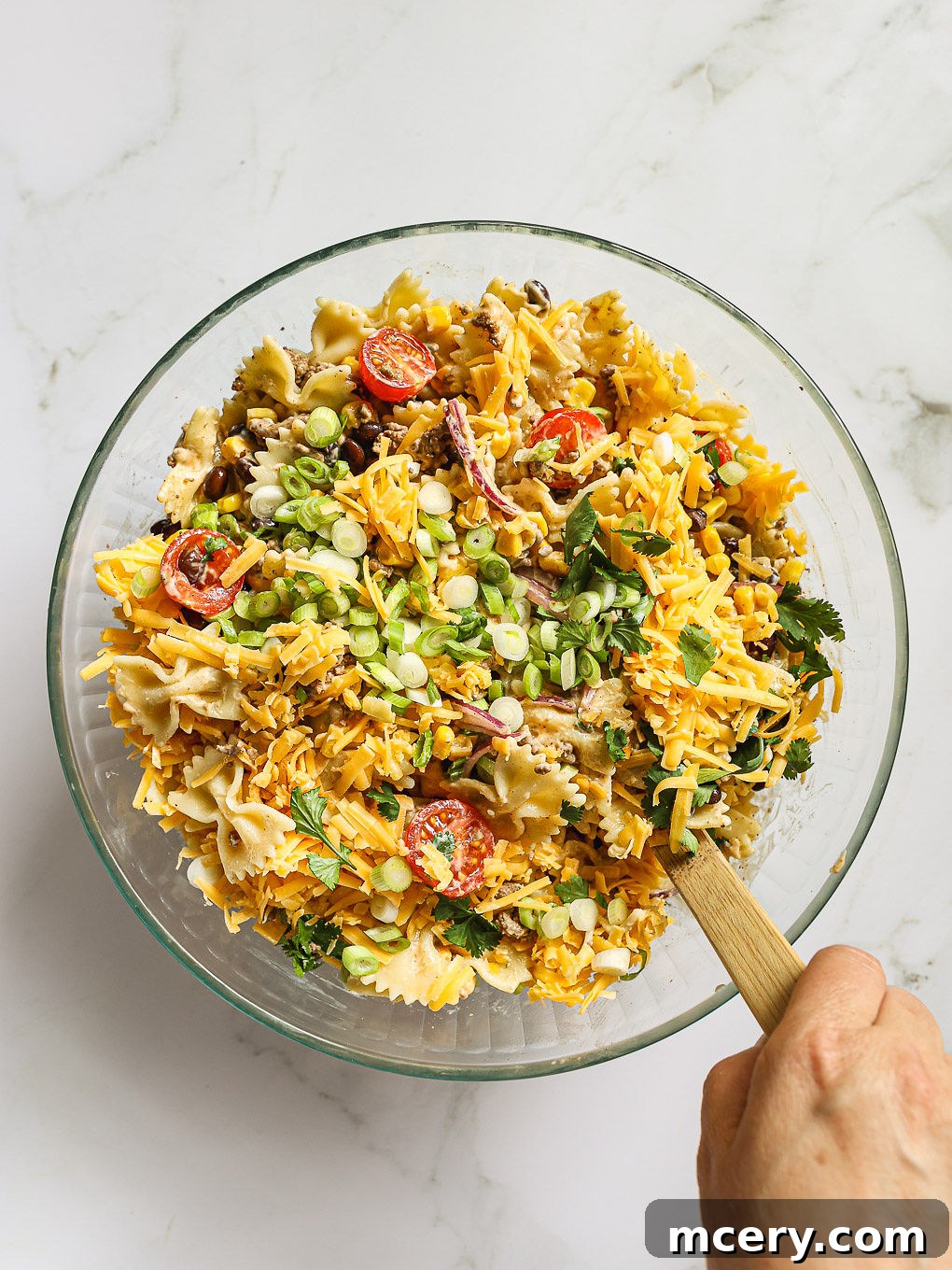 The finished Cowboy Pasta Salad tossed with dressing, cheese, scallions, and cilantro in a glass bowl, ready to be served.