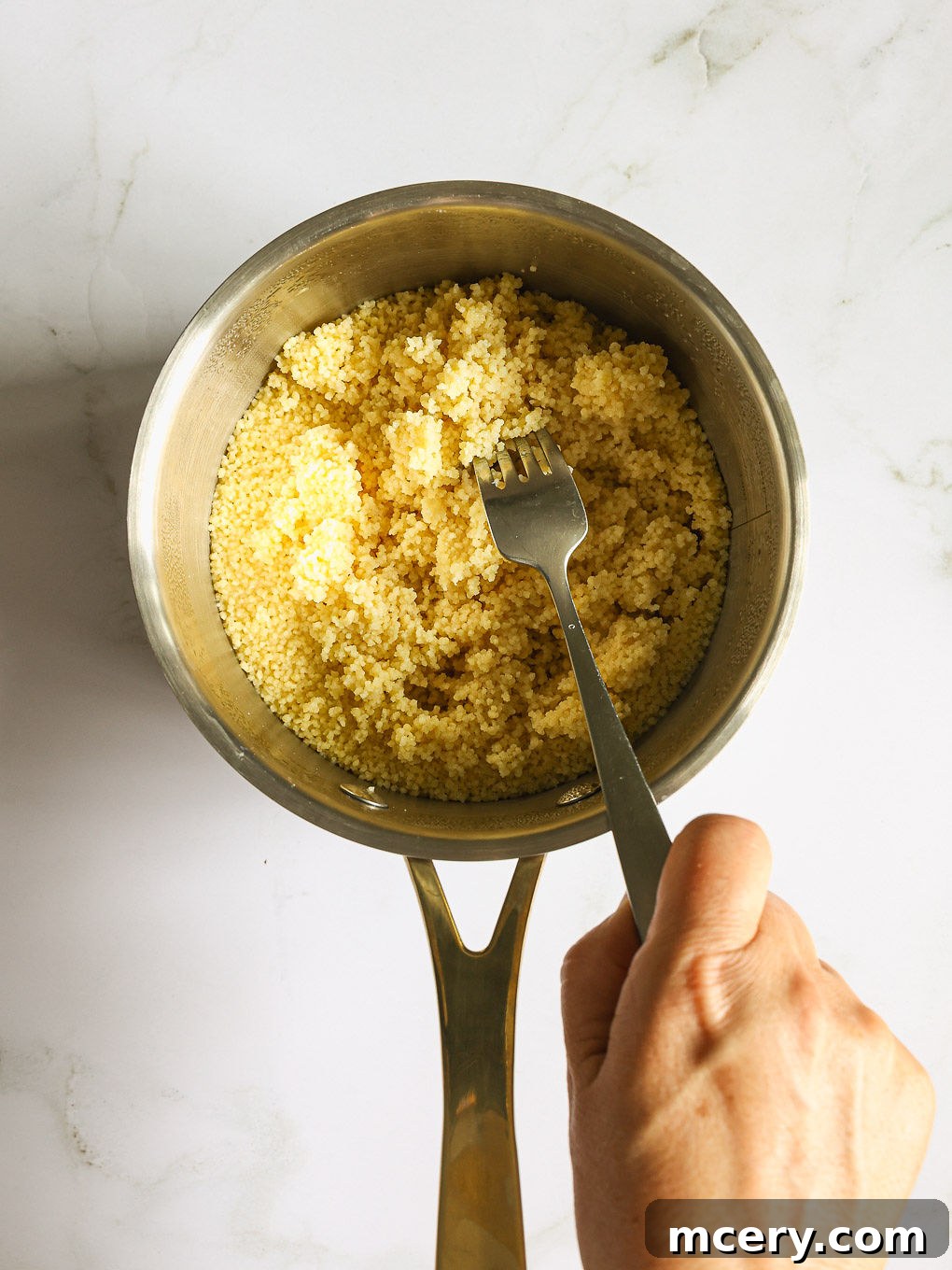 cooked couscous fluffed in a pan.