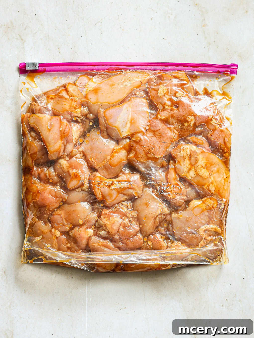 Uniformly cut chicken pieces being added to the zip-top bag with the prepared marinade.