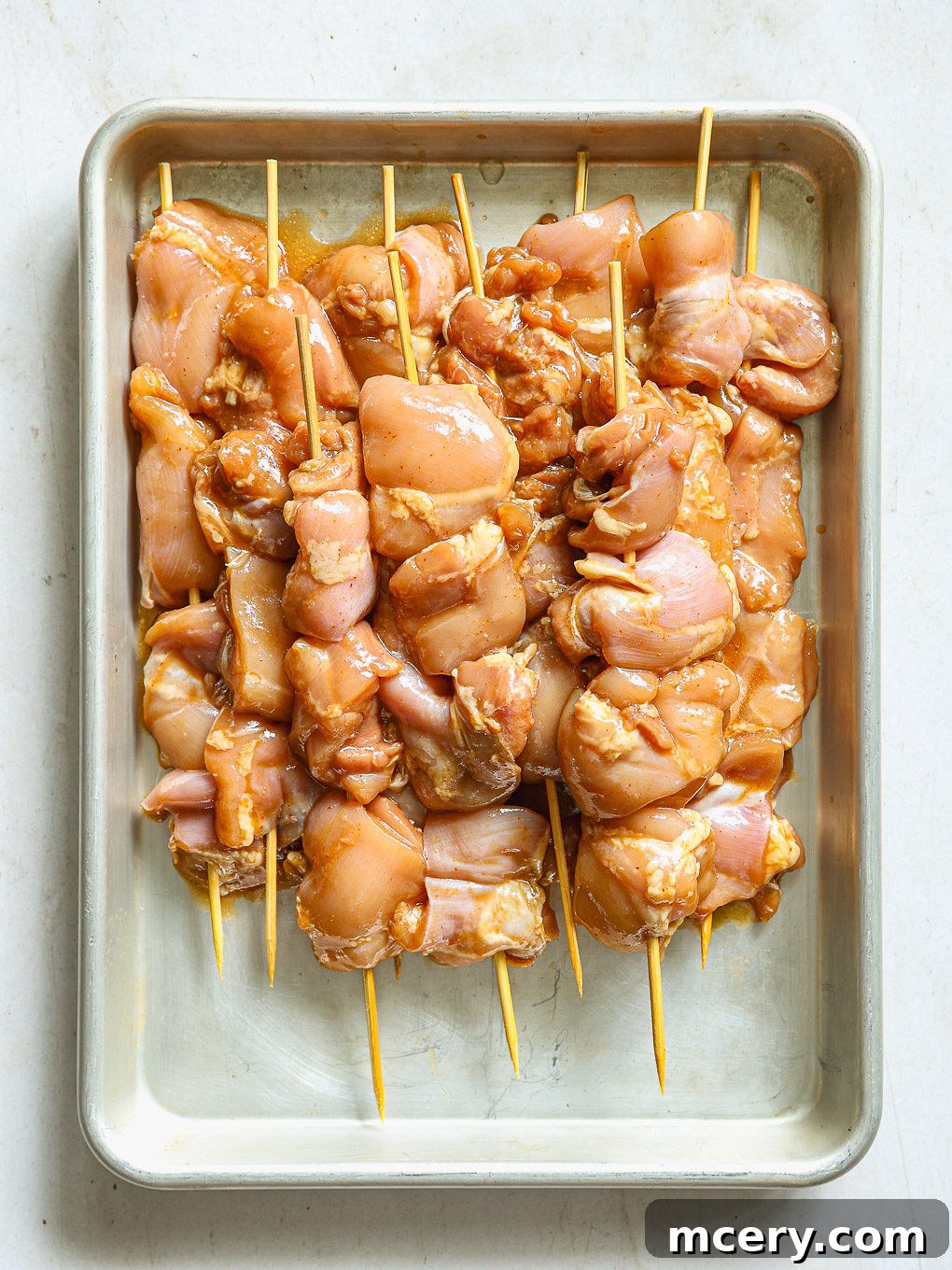 Marinated chicken pieces carefully threaded onto long metal skewers, ready for grilling.