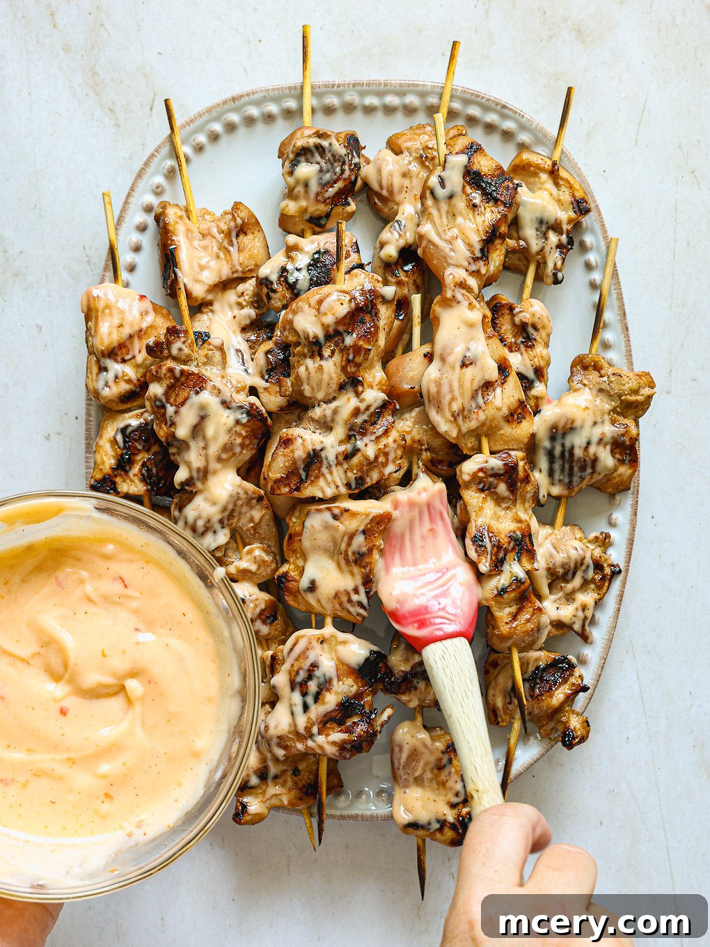 Freshly grilled chicken skewers artfully arranged on a serving platter, generously brushed with the creamy Bang Bang sauce and sprinkled with fresh cilantro.