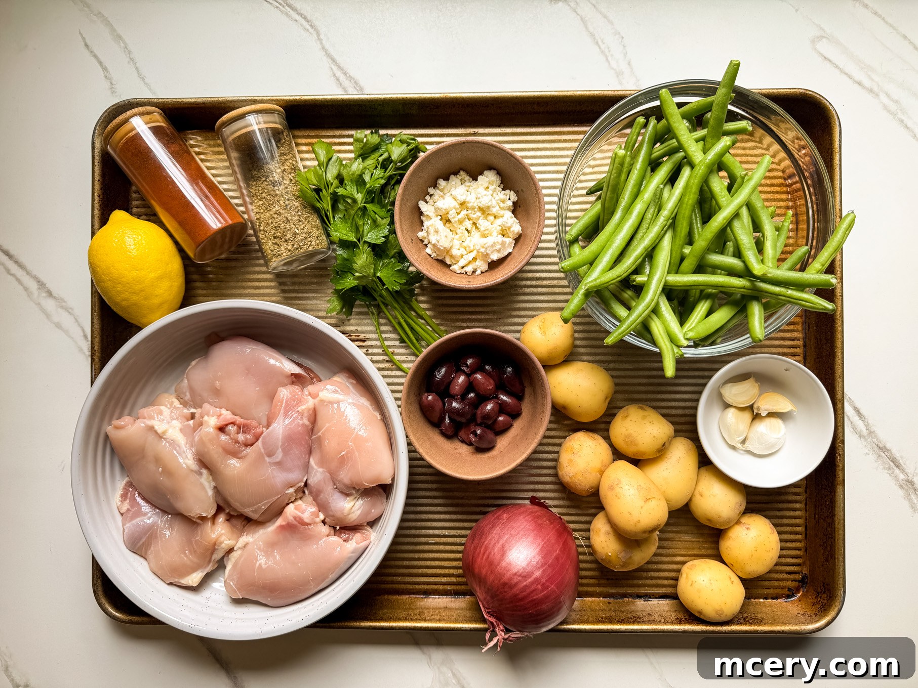Sheet Pan Lemon Chicken and Mediterranean Vegetables 3 Individual ingredients laid out for one pan Mediterranean chicken: chicken, potatoes, green beans, olives, feta, lemon, herbs, garlic.