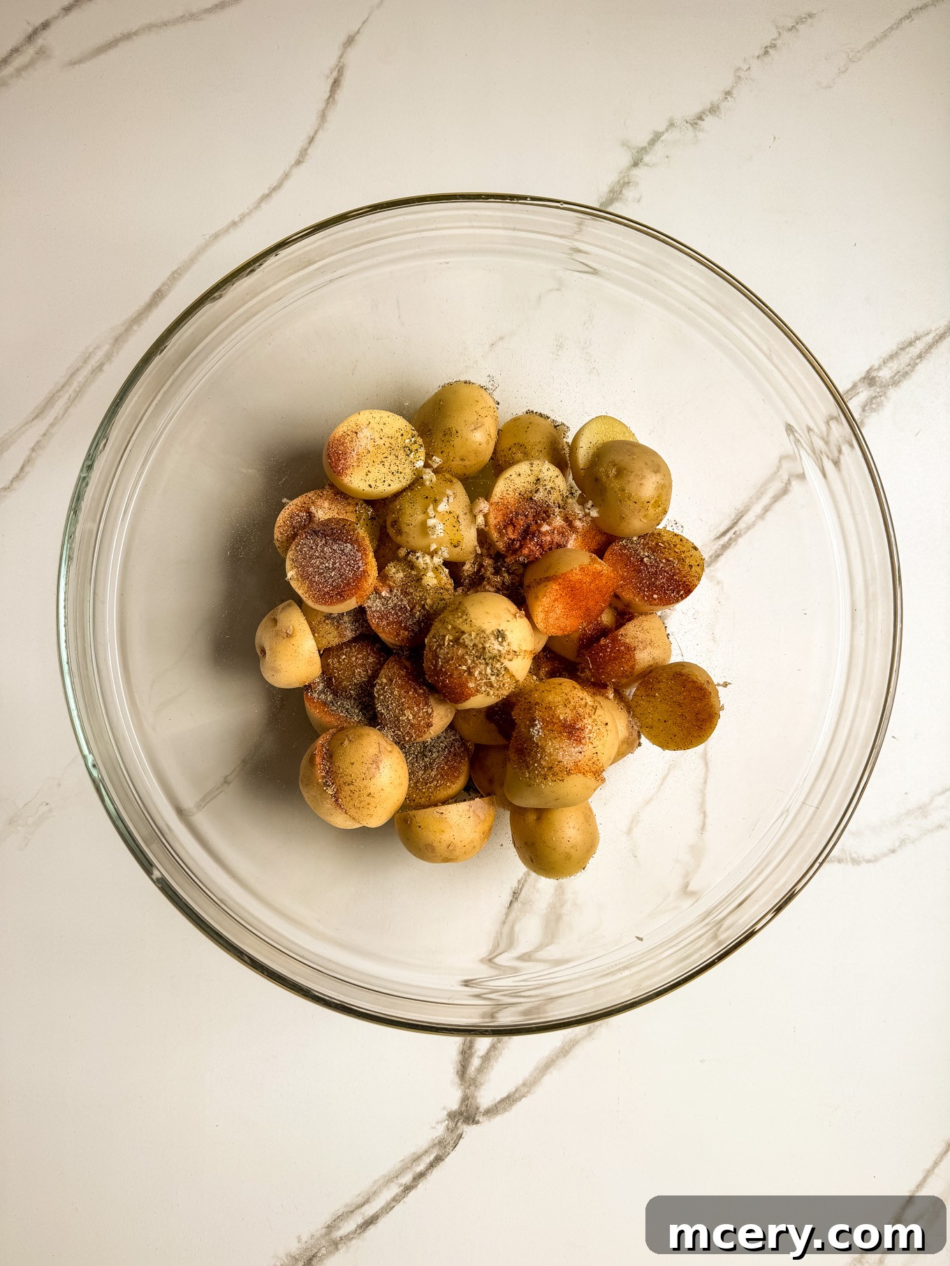 Sheet Pan Lemon Chicken and Mediterranean Vegetables 4 Halved baby potatoes tossed with olive oil, minced garlic, and spices in a glass mixing bowl.