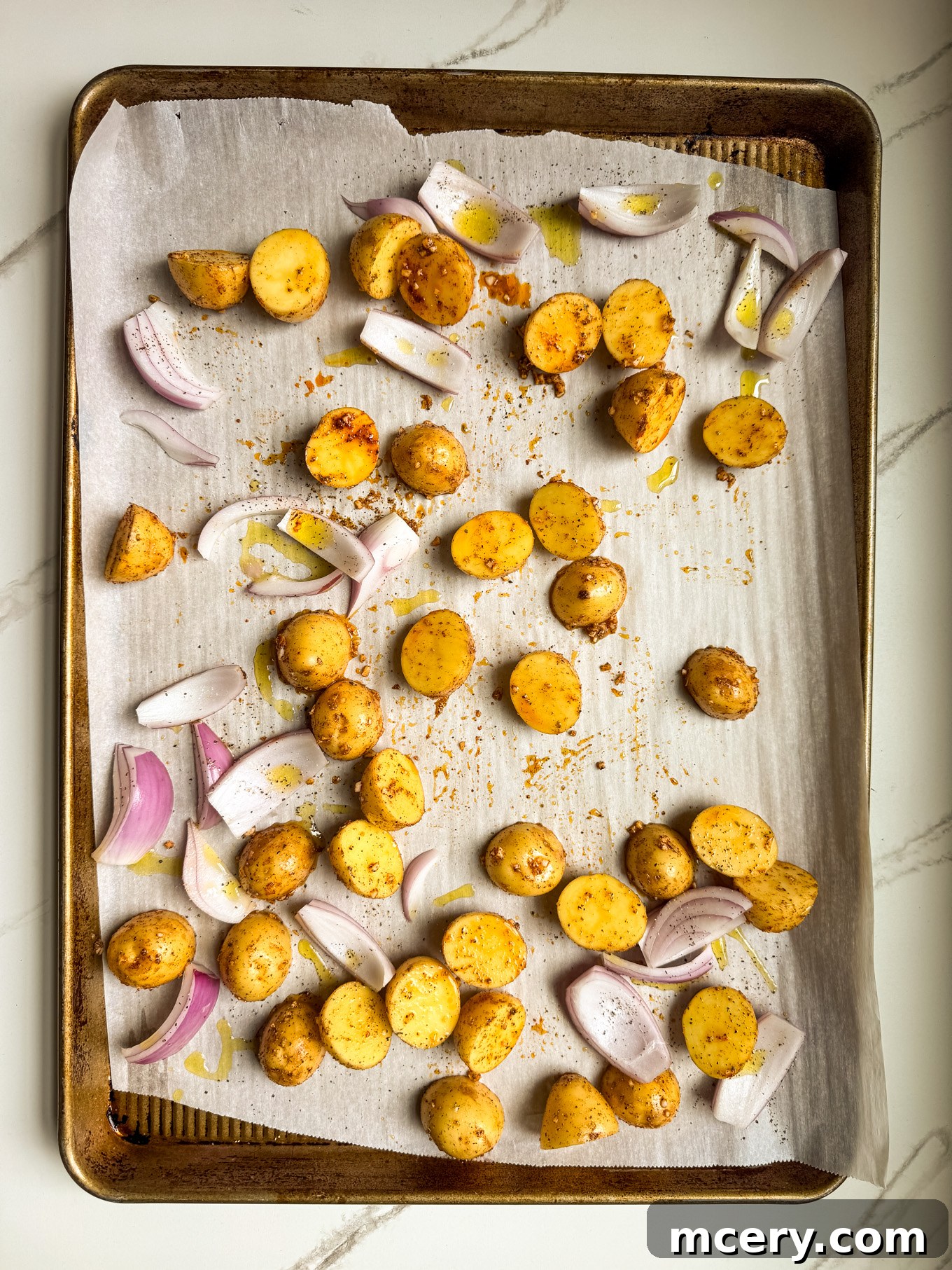 Sheet Pan Lemon Chicken and Mediterranean Vegetables 5 Halved potatoes and red onion wedges spread in a single layer on a sheet pan, ready for roasting.
