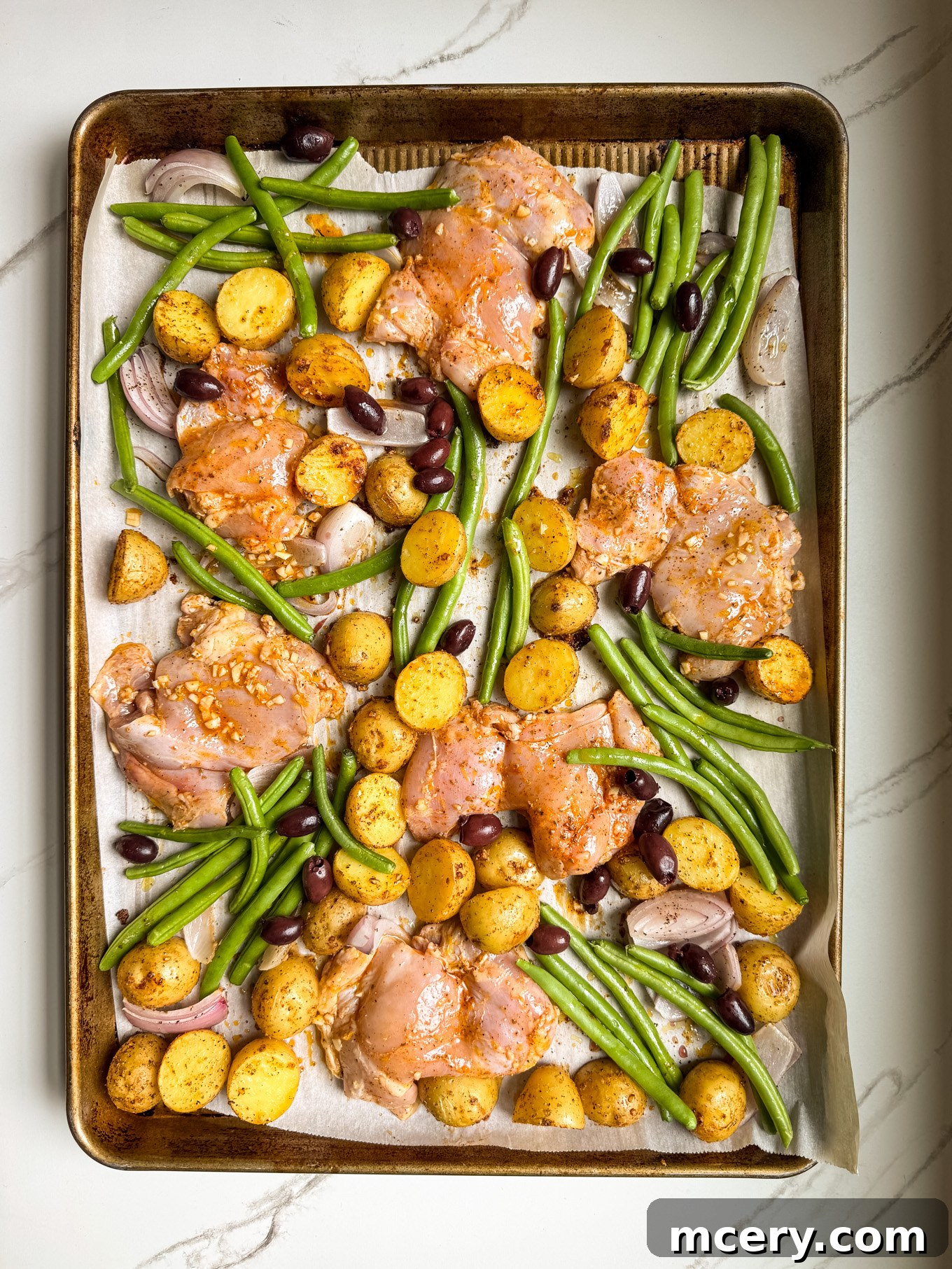 Sheet Pan Lemon Chicken and Mediterranean Vegetables 6 Chicken thighs nestled among roasted potatoes and green beans with olives on a sheet pan.