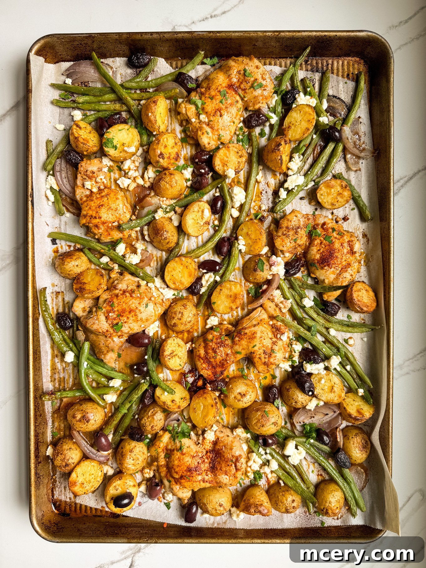 Sheet Pan Lemon Chicken and Mediterranean Vegetables 7 Roasted chicken, potatoes, green beans, and olives sprinkled with crumbled feta cheese on a sheet pan.