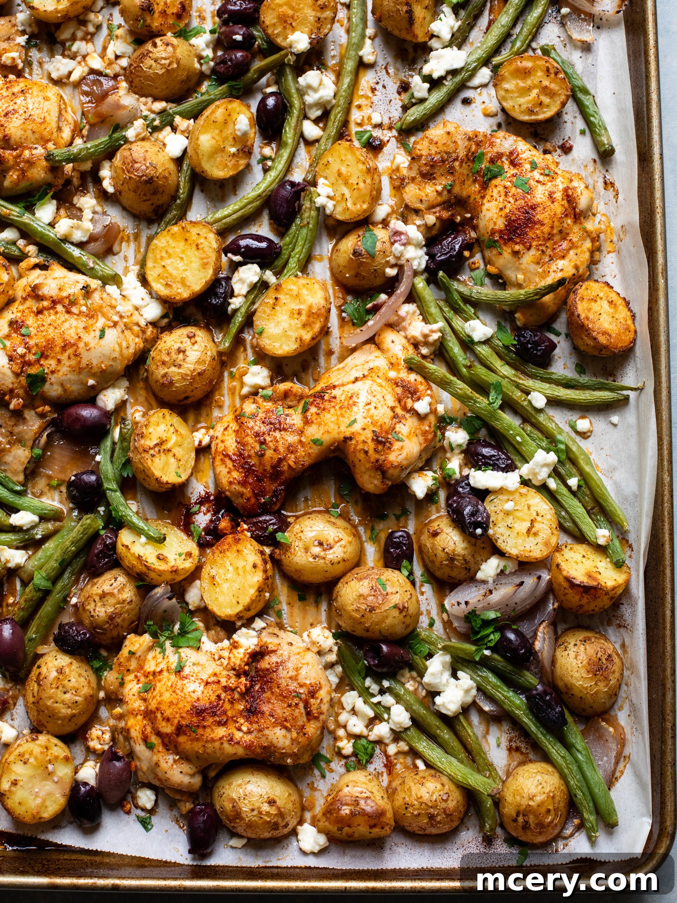 Sheet Pan Lemon Chicken and Mediterranean Vegetables 8 Close-up shot of roasted Mediterranean lemon chicken, potatoes, green beans, olives, and feta on a sheet pan, garnished with fresh parsley.