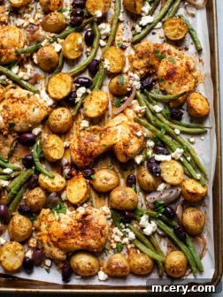 Close up of roasted Mediterranean lemon chicken with potatoes and green beans on a sheet pan, garnished with fresh parsley.