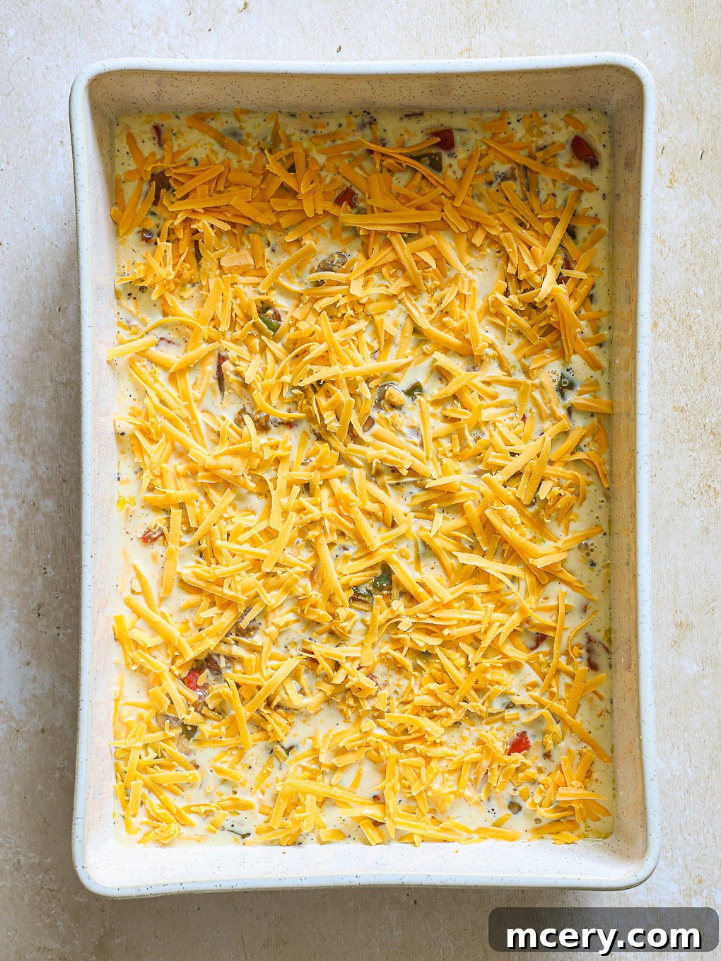 Overnight Southwest Fiesta Bake 9 egg mixture topped with shredded cheese, ready to bake.