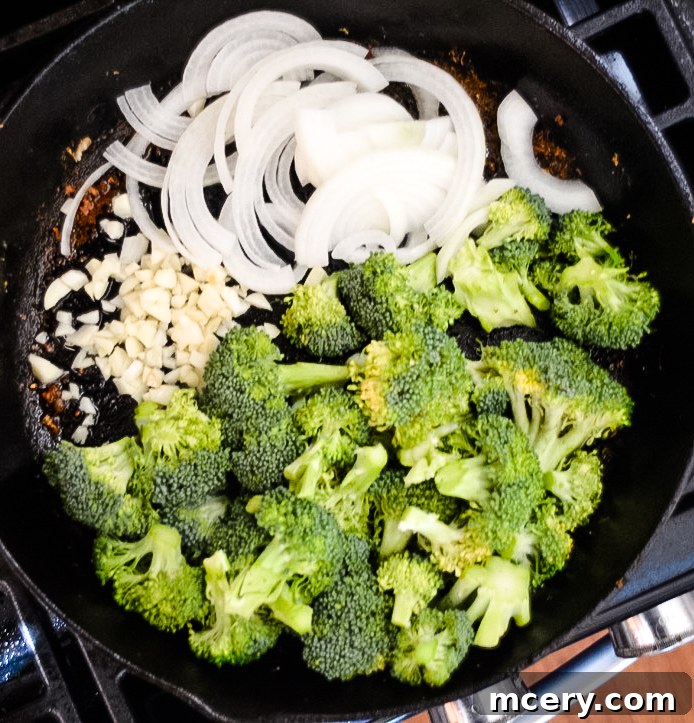 Savory Chicken and Broccoli Stir-Fry 5 Fresh broccoli florets and sliced white onions are being stir-fried in a large pan or wok. The vegetables are vibrant and appear to be cooking to a crisp-tender consistency, preparing them for the sauce.