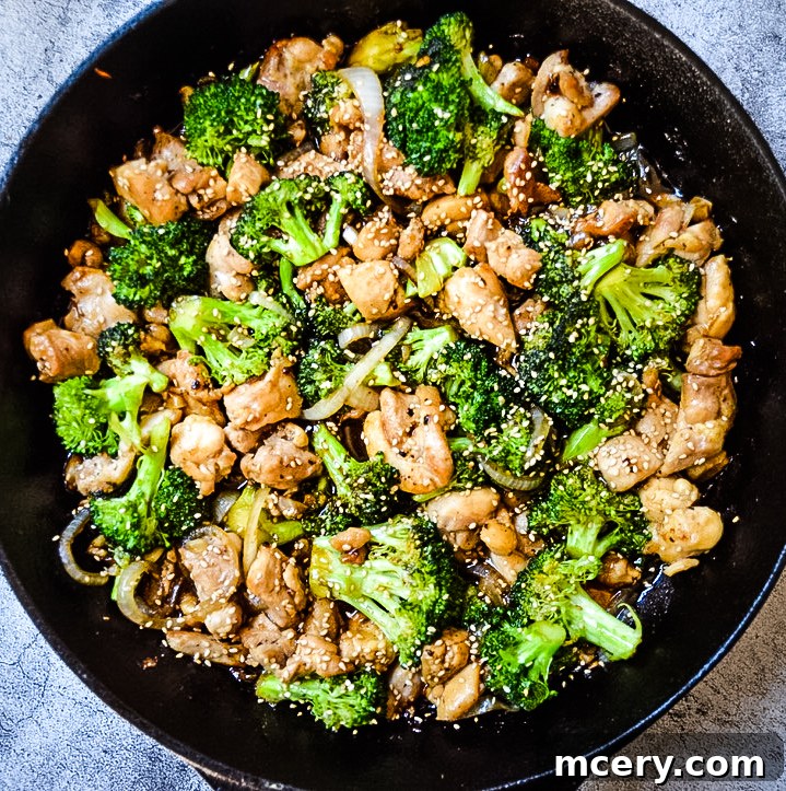 Savory Chicken and Broccoli Stir-Fry 6 A close-up view of a serving of Chicken and Broccoli Stir Fry presented over white rice, garnished with sesame seeds. The glossy sauce coats the chicken and broccoli, making it look incredibly appetizing and ready to be enjoyed.