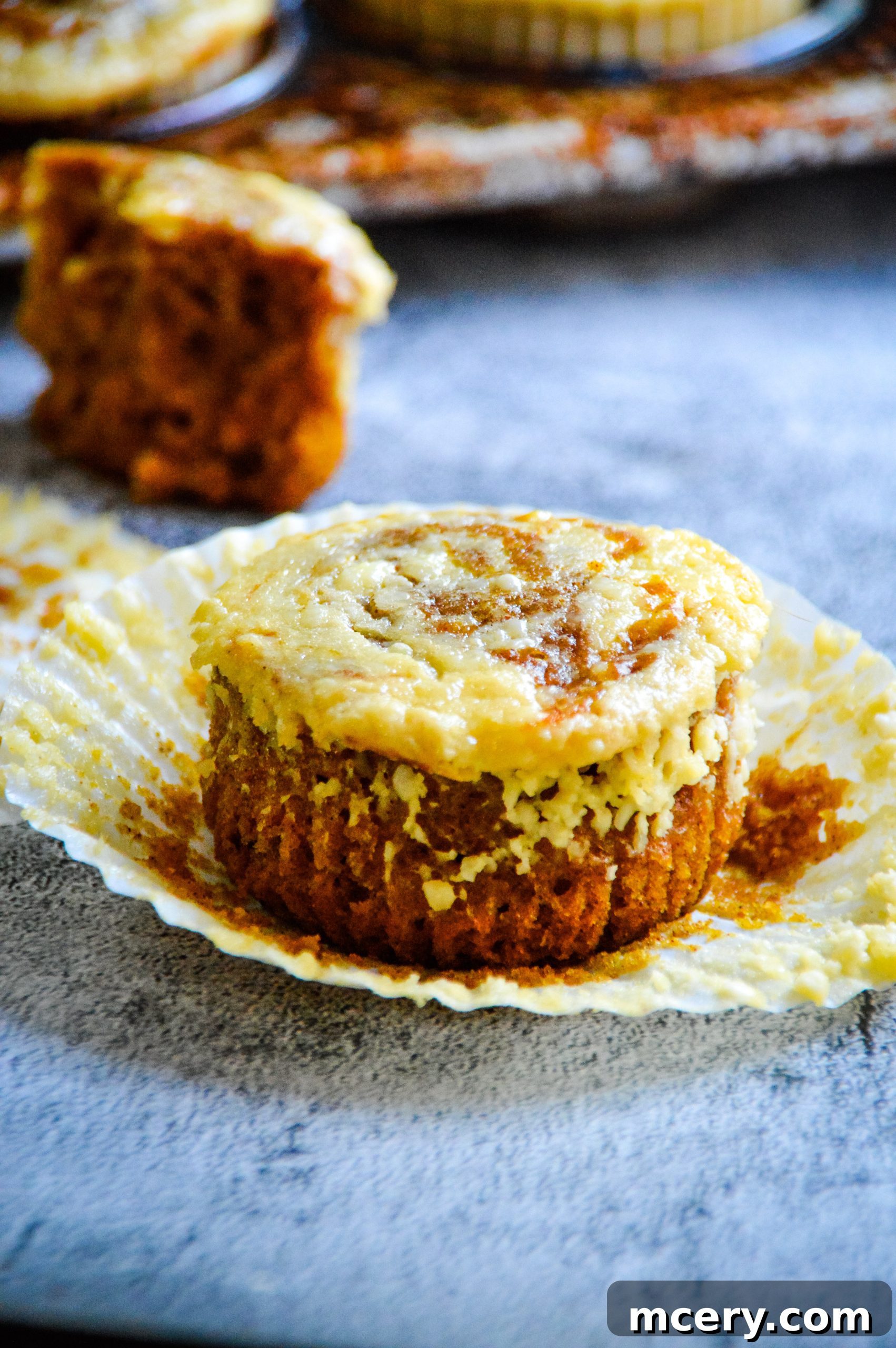 Pumpkin Cheesecake Swirl Muffins 3 A close-up shot of a single pumpkin cream cheese swirl muffin, showcasing its golden-brown top, moist interior, and the distinct swirl of cream cheese, ready to be enjoyed.