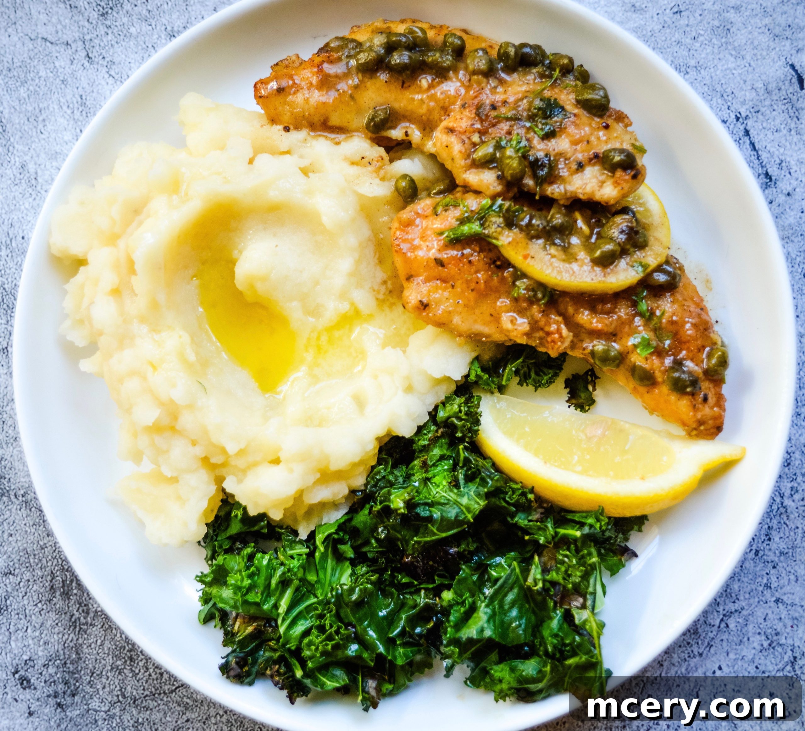 Effortless Chicken Piccata 3 Close-up of golden-brown chicken piccata on a white plate, showing the rich lemon caper sauce with visible capers and a hint of parsley garnish.