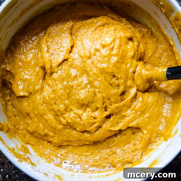 Close-up of wet ingredients being whisked in a bowl, showing pumpkin puree, eggs, and oils blending together for the bread batter.