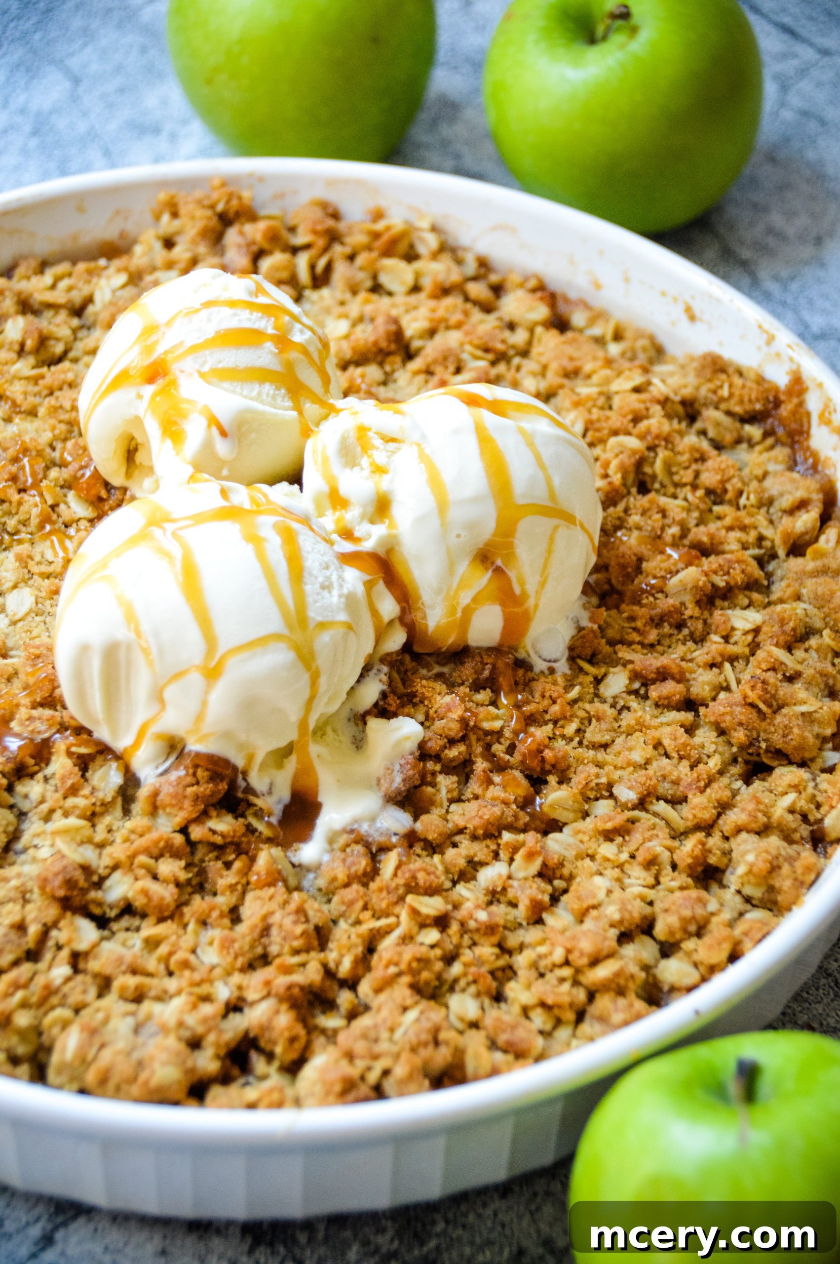 Close-up of a golden-brown apple crisp in a baking dish, showing a crumbly oat topping and soft apple filling underneath.