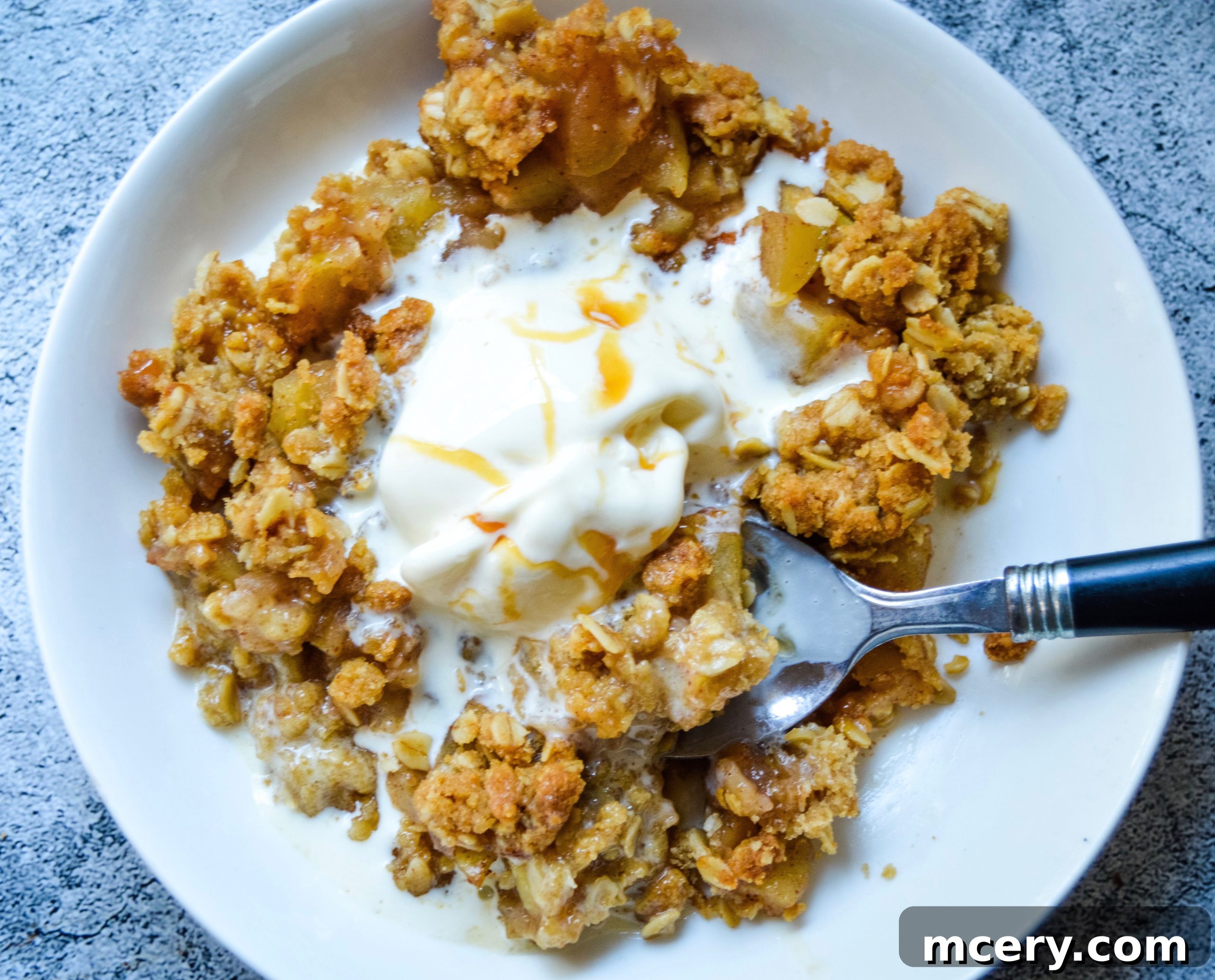 Apple crisp baking in a rectangular dish, with the top golden and bubbly, surrounded by kitchen towel on a wooden surface.