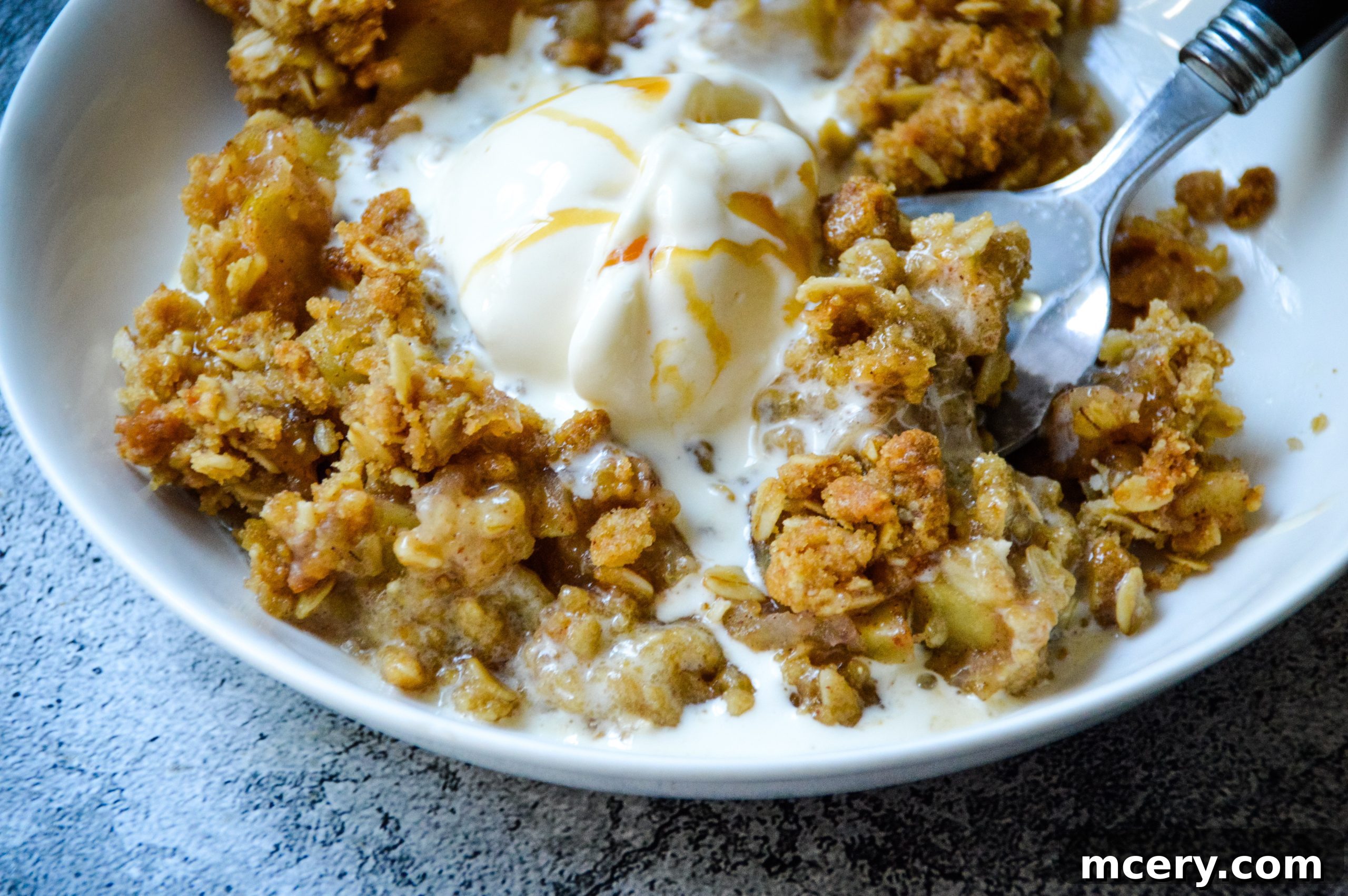 Freshly baked apple crisp in a round baking dish, topped with three scoops of vanilla ice cream and drizzled with caramel sauce, ready to be served.