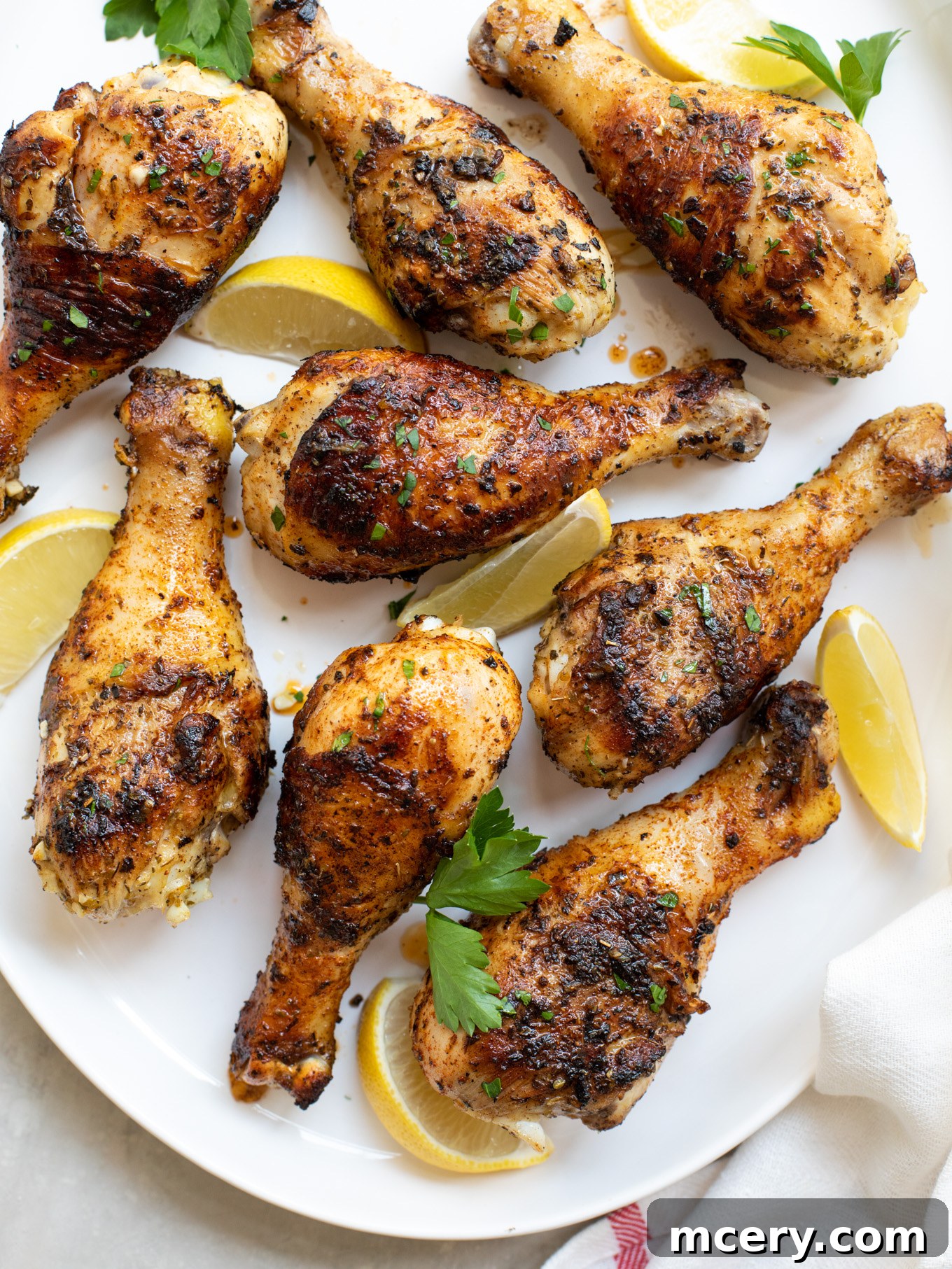 Smoky Grilled Chicken Drumsticks 2 Grilled chicken drumsticks perfectly cooked and arranged on a white platter, garnished with fresh parsley and bright lemon wedges.