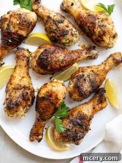 Grilled chicken drumsticks on a white platter garnished with parsley and lemons.