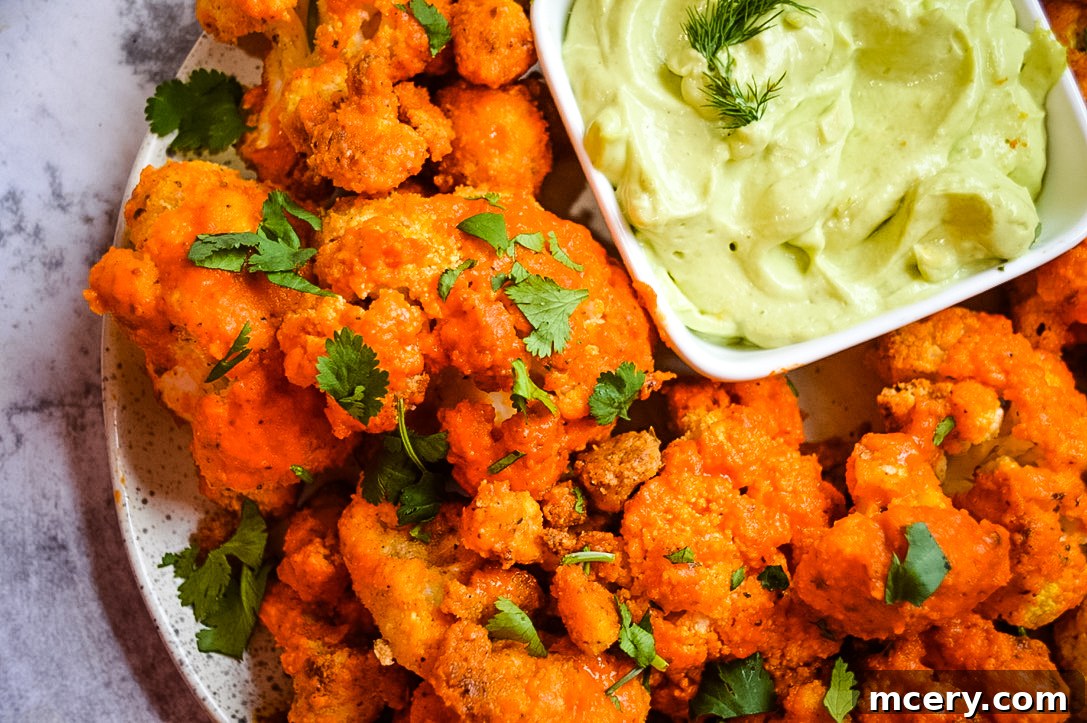 A close-up of golden brown Buffalo Cauliflower Bites on a plate with a side of creamy green avocado dip, ready to be enjoyed.