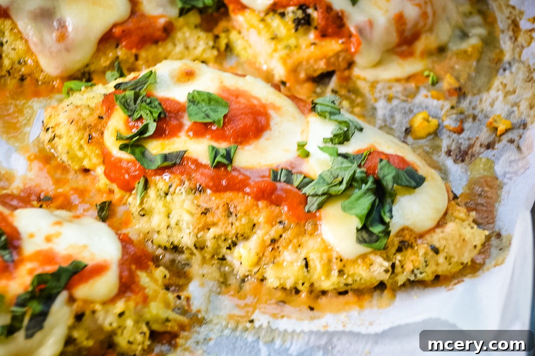 Crispy Keto Chicken Parmesan Bake 4 Three pieces of cooked Keto Baked Chicken Parmesan on a baking sheet, garnished with fresh basil.