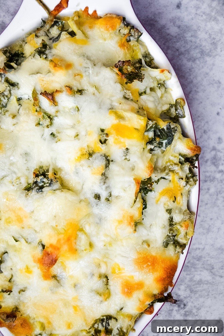 Kickin' Chunky Artichoke Jalapeño Dip 4 A top-down view of the Chunky Jalapeño Artichoke Dip mixture in a mixing bowl before baking, showcasing the vibrant green flecks of kale and spinach intertwined with creamy cheese and artichoke pieces.