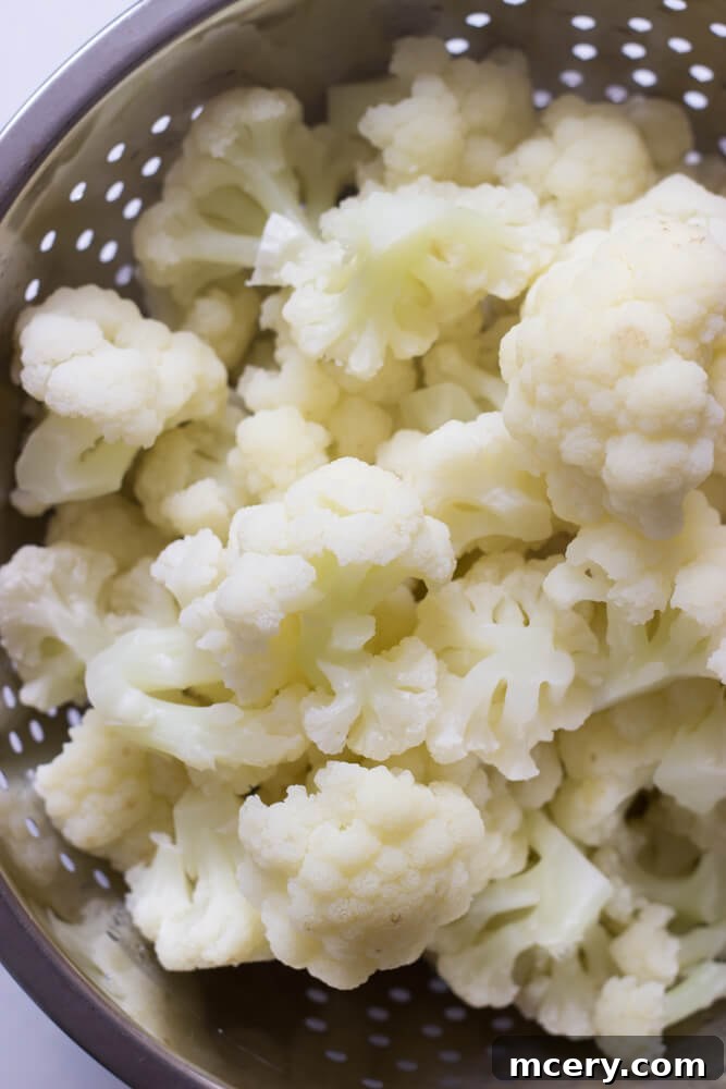 Steaming cooked cauliflower florets in a colander after boiling.