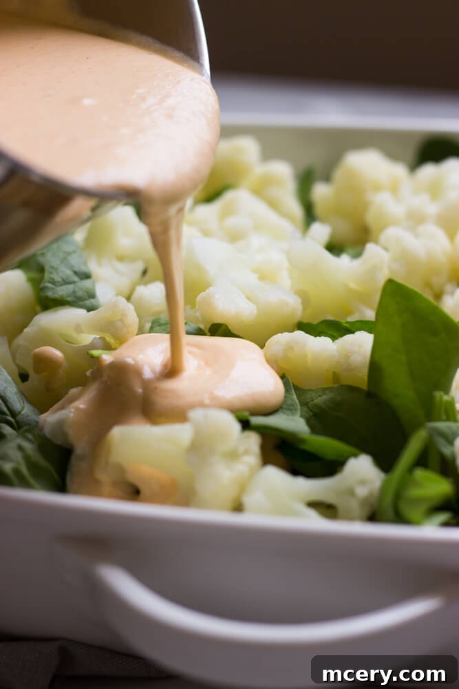 Finished cauliflower spinach casserole, golden brown and bubbly, in a white baking dish.