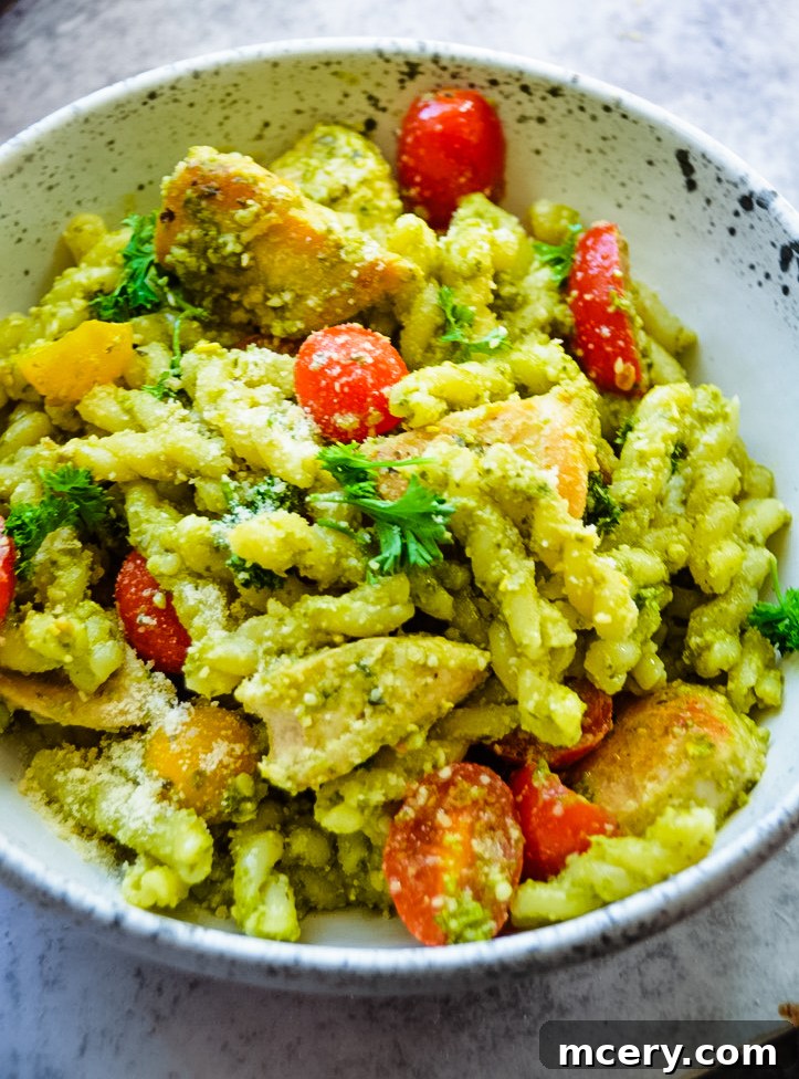 A bowl of Chicken Pesto Pasta with a vibrant green pesto sauce, cherry tomatoes, and garnished with fresh parsley.