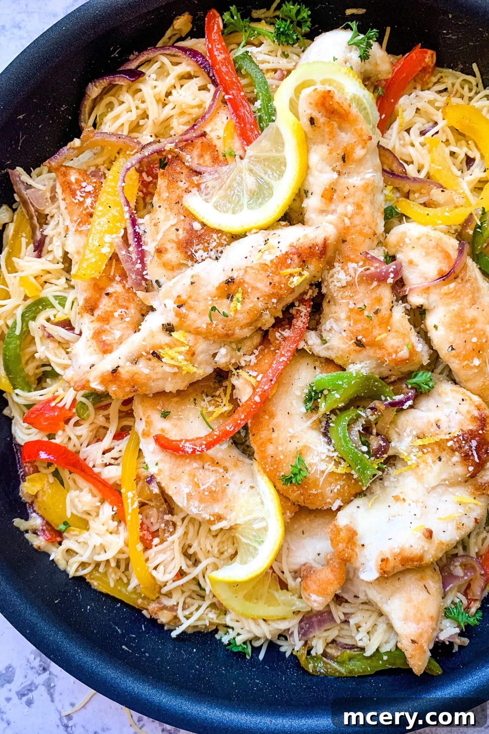 Lemon Garlic Chicken Scampi Pasta 3 A top-down view of a serving of Easy Chicken Scampi Pasta, showing the chicken, colorful peppers, and pasta tangled together, garnished with fresh herbs and lemon slices.